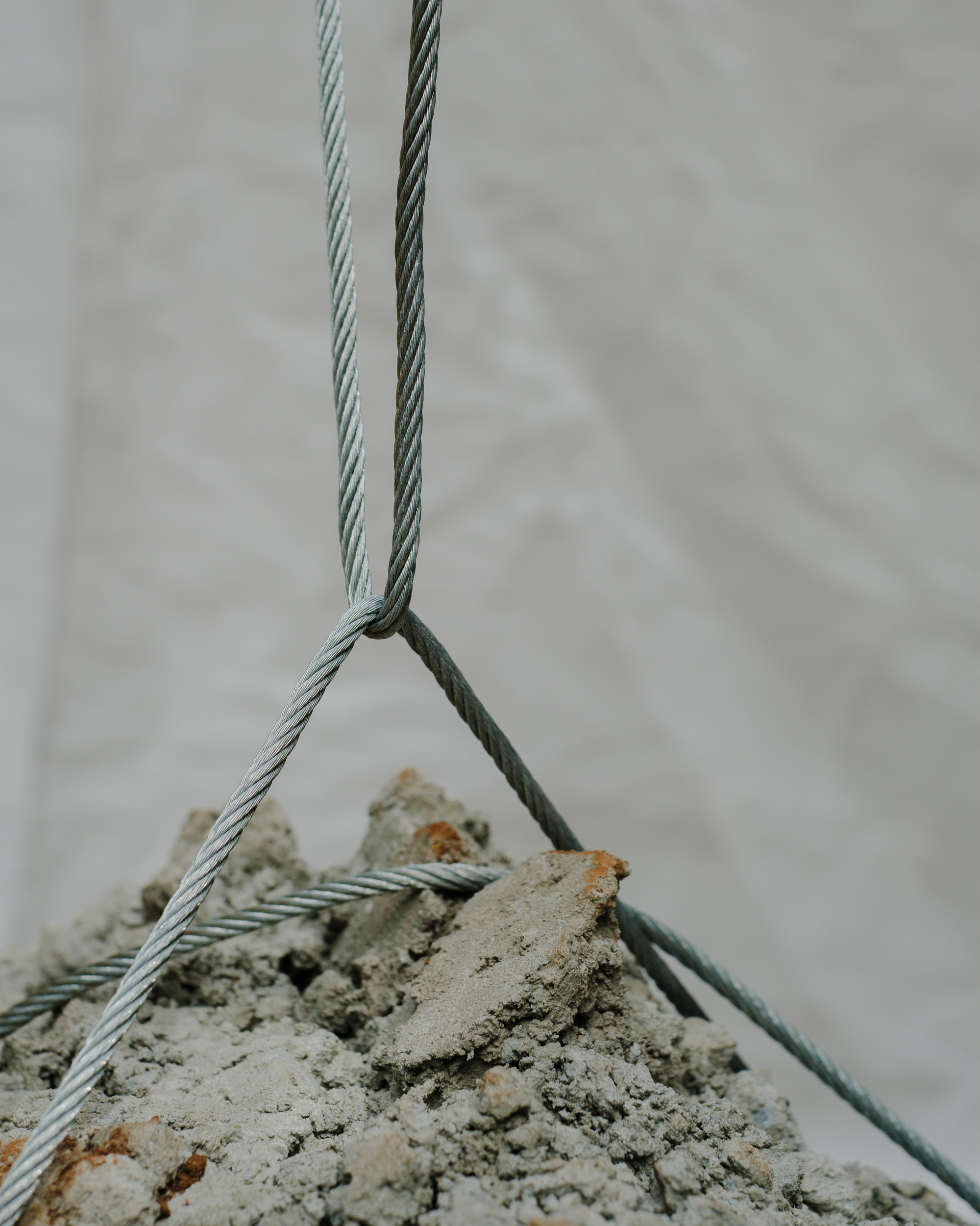 Steel cables securing a rough concrete block suspended against a white fabric backdrop