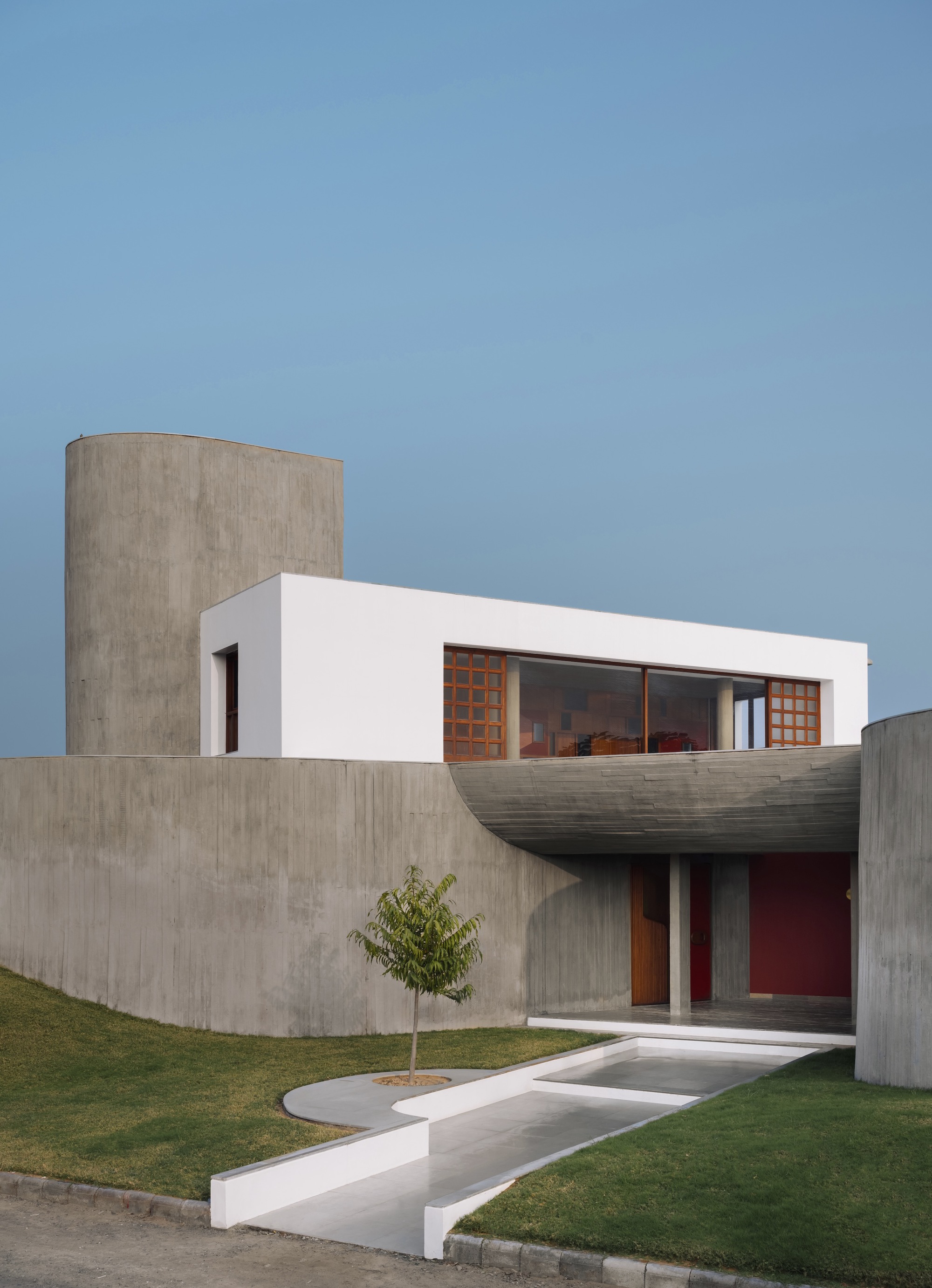 Entrance facade combining board-formed concrete walls with a white rendered upper volume and young tree