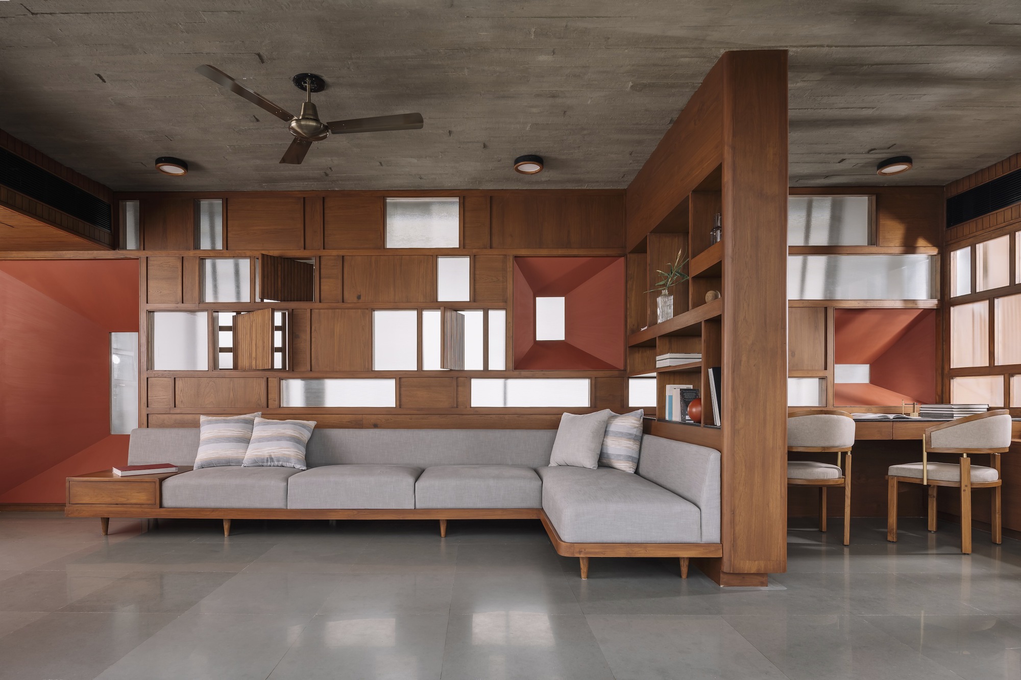 Living room with grey sectional sofa below a gridded timber and terracotta wall system with recessed lighting