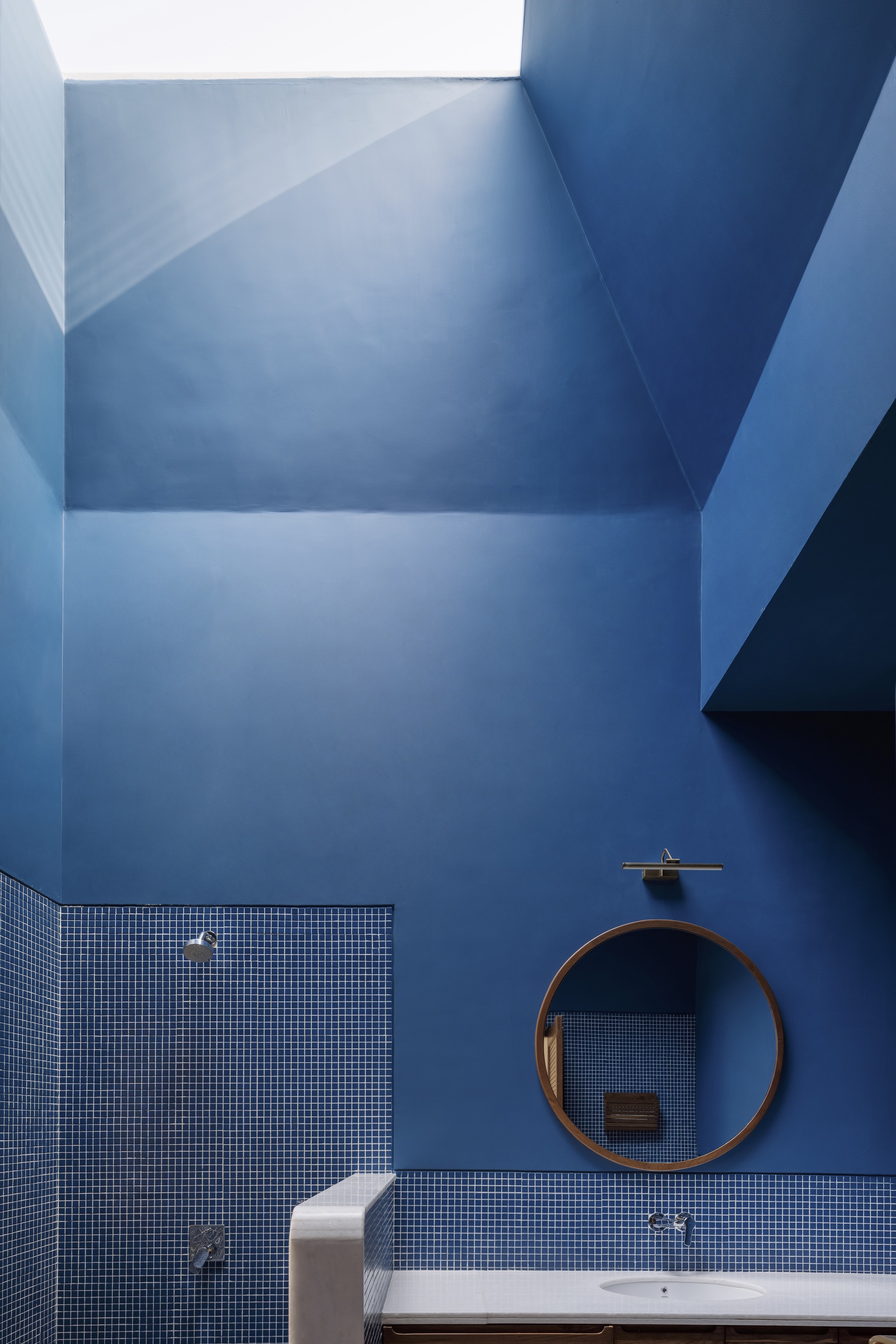 Bathroom skylight well with blue painted surfaces above mosaic tile walls and circular mirror