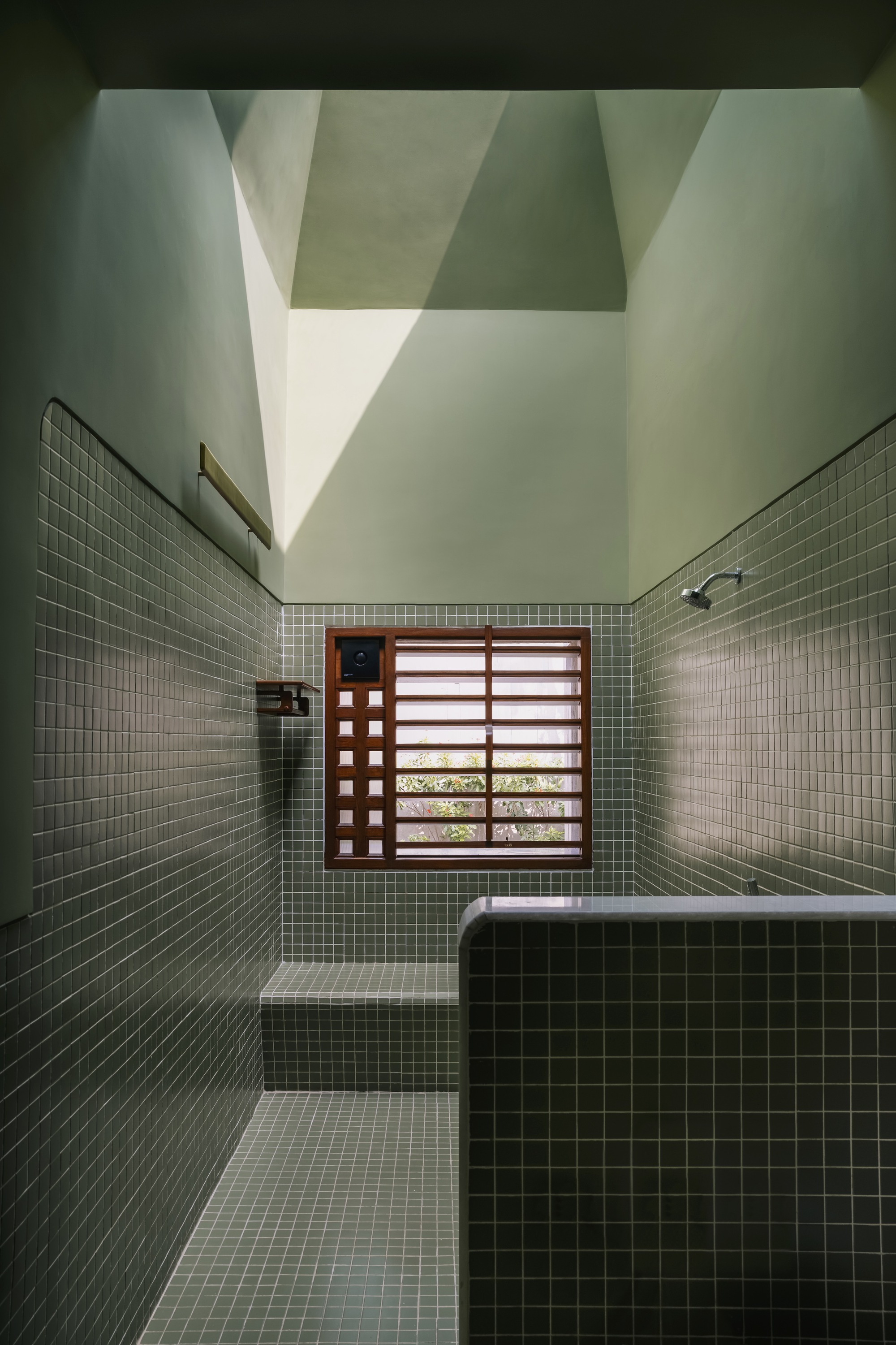 Tiled bathing room with timber louvered window and pyramidal skylight casting shadow patterns