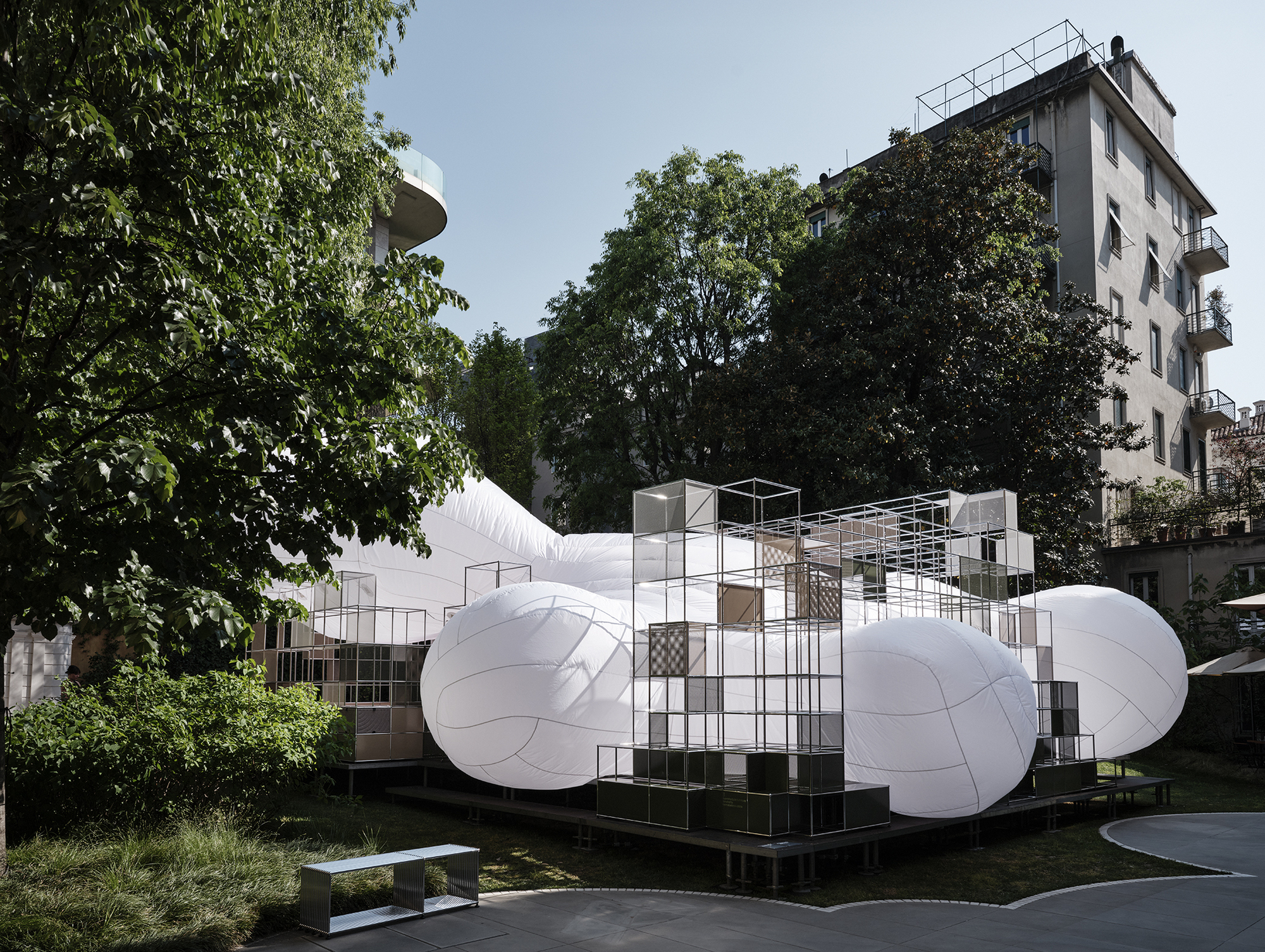 White inflated sculptural volumes anchored by a central steel grid scaffold structure in a courtyard