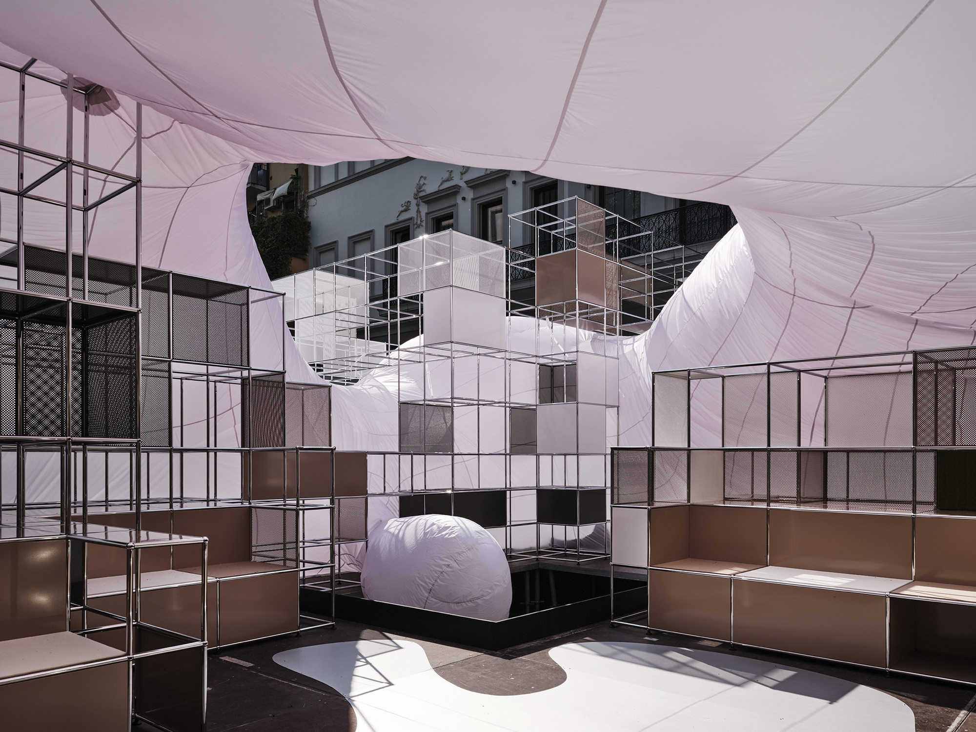 Interior view beneath the tensioned fabric canopy with modular steel shelving and white cube tower element