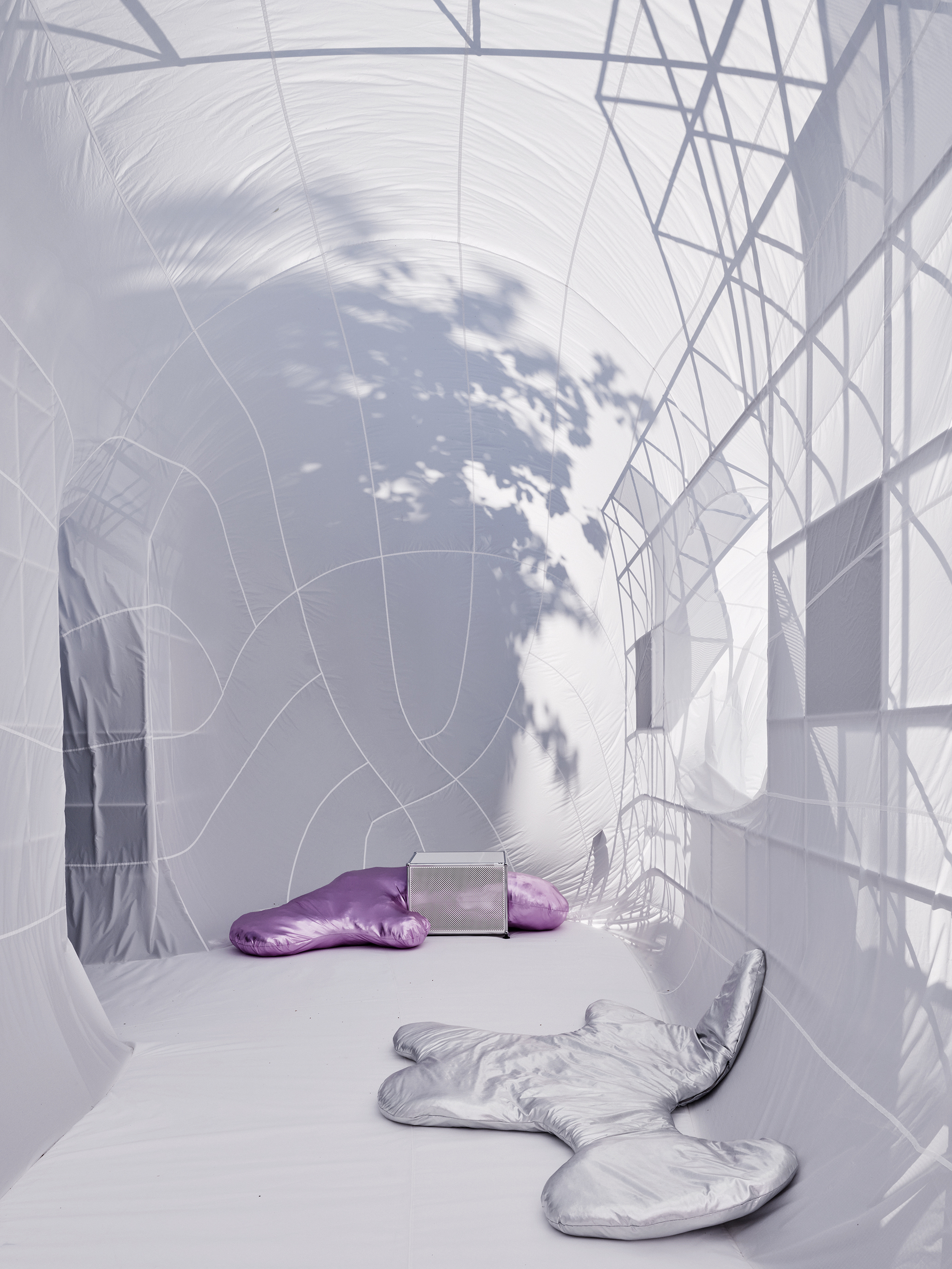 White fabric chamber with tree shadow cast across the membrane surface and two silver cushions on floor