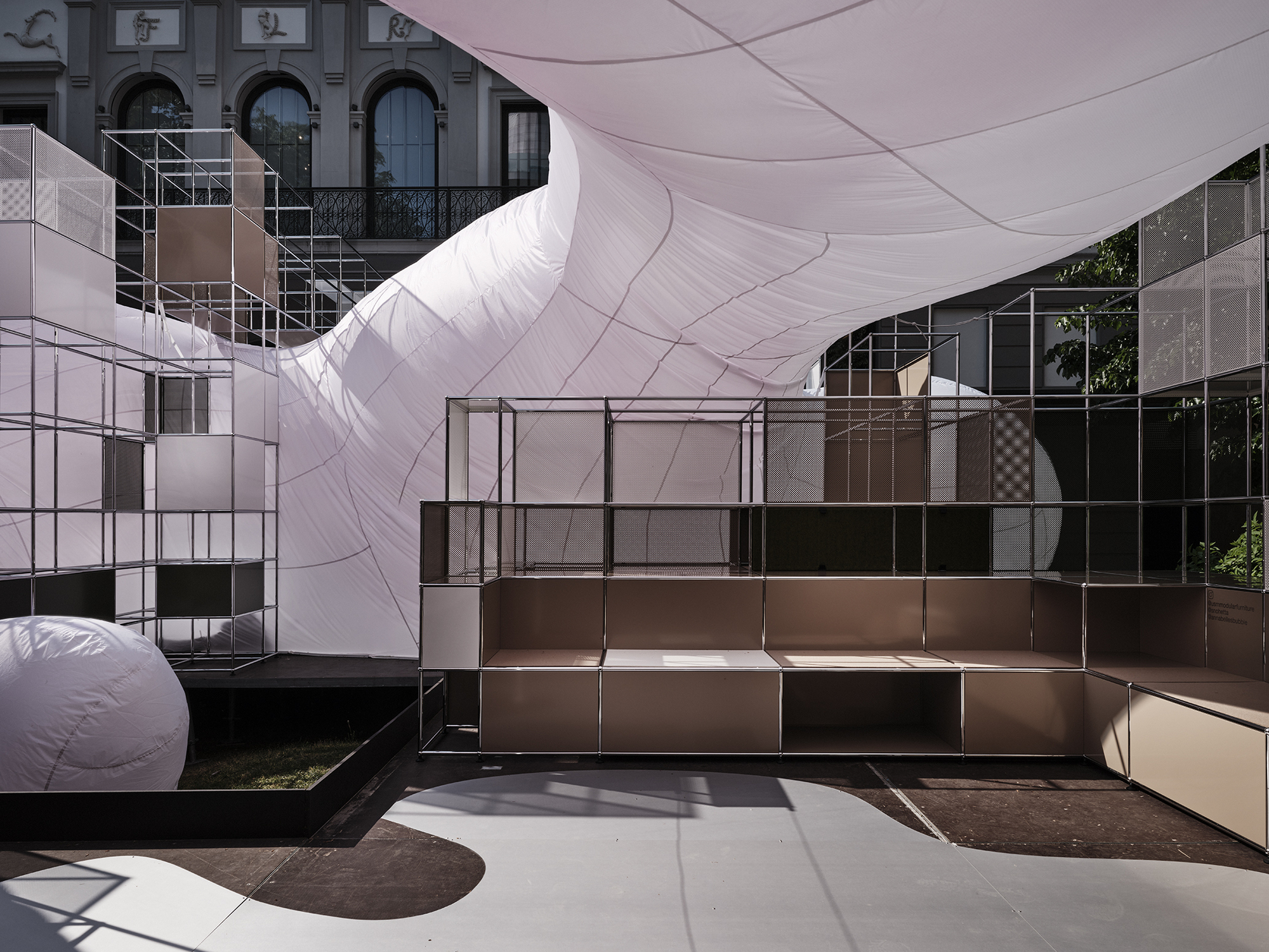 Modular bronze and glass shelving units positioned beneath the curved inflatable canopy casting shadows