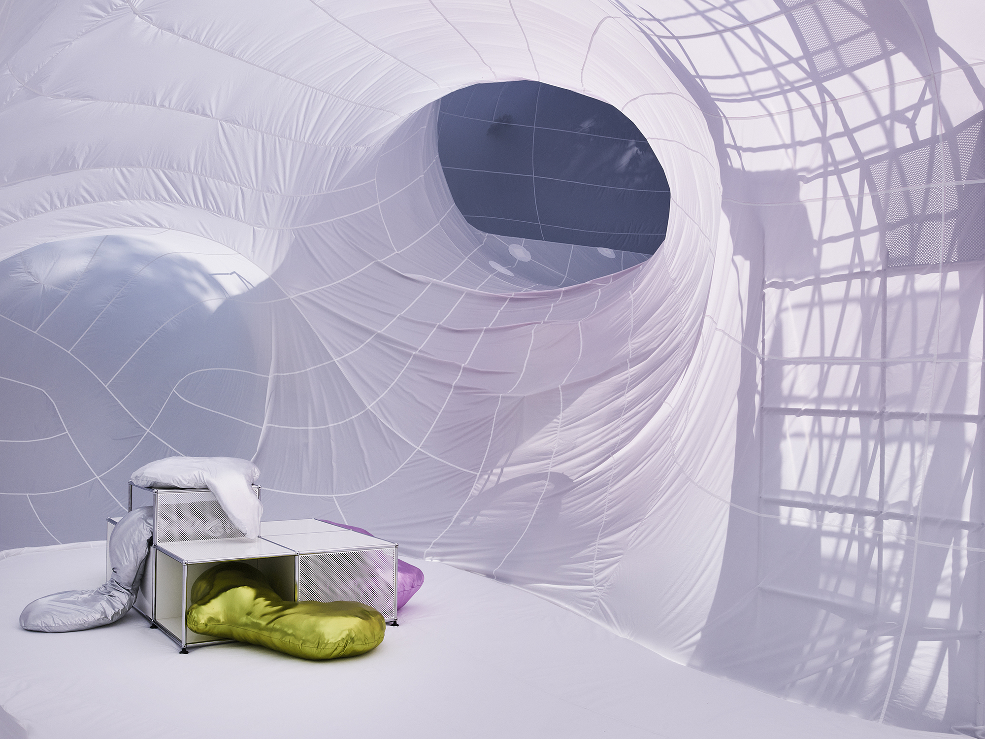 Inflatable chamber with a circular portal and yellow cushions beside metal furniture under soft light
