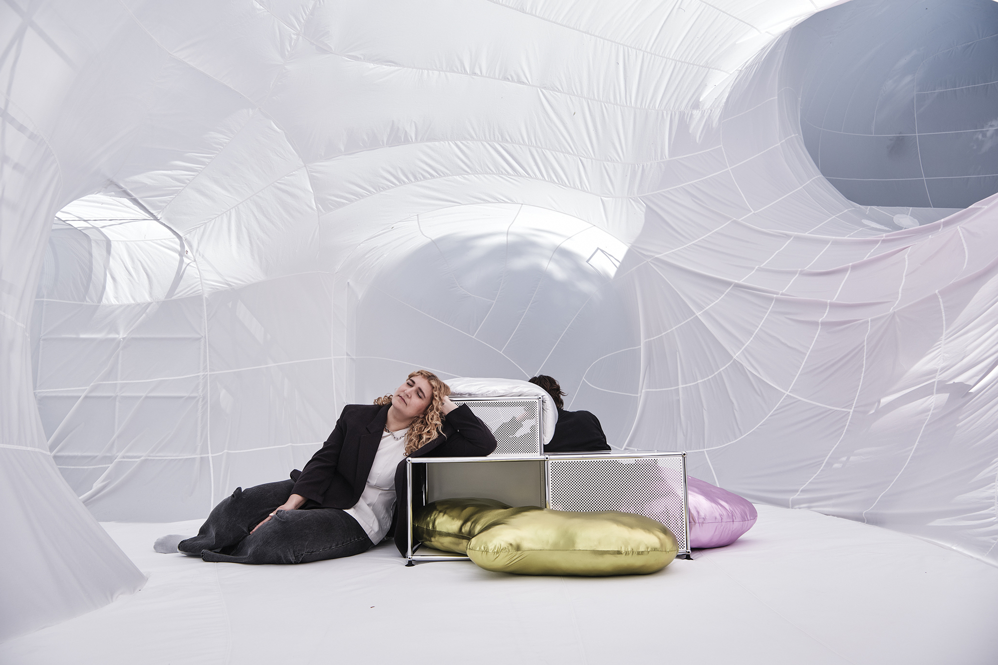 Interior view of white inflatable structures with a person reclining beside metal shelving and gold cushions