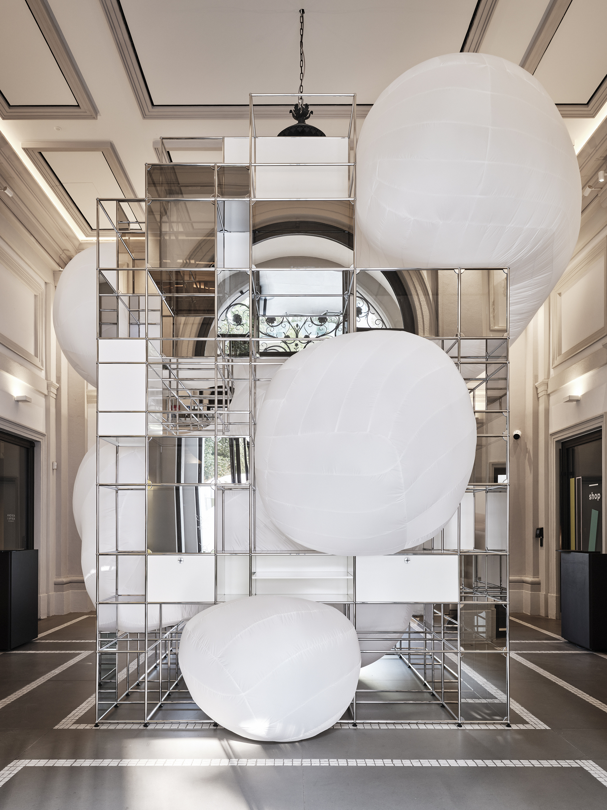 Double-height lobby with suspended white spherical balloons in front of mirrored metal grid storage tower