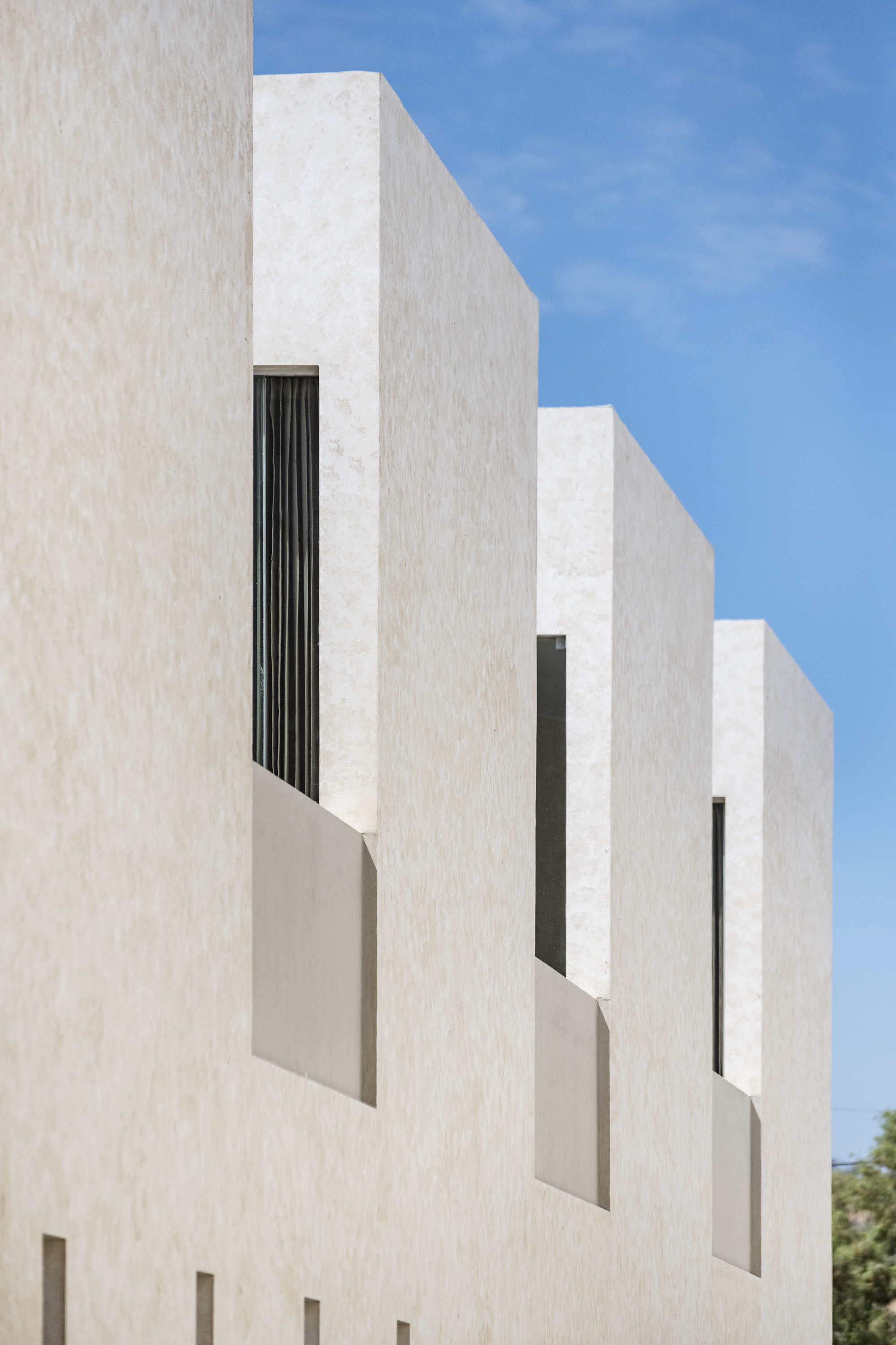 Stepped white facade with recessed vertical window openings against a clear blue sky