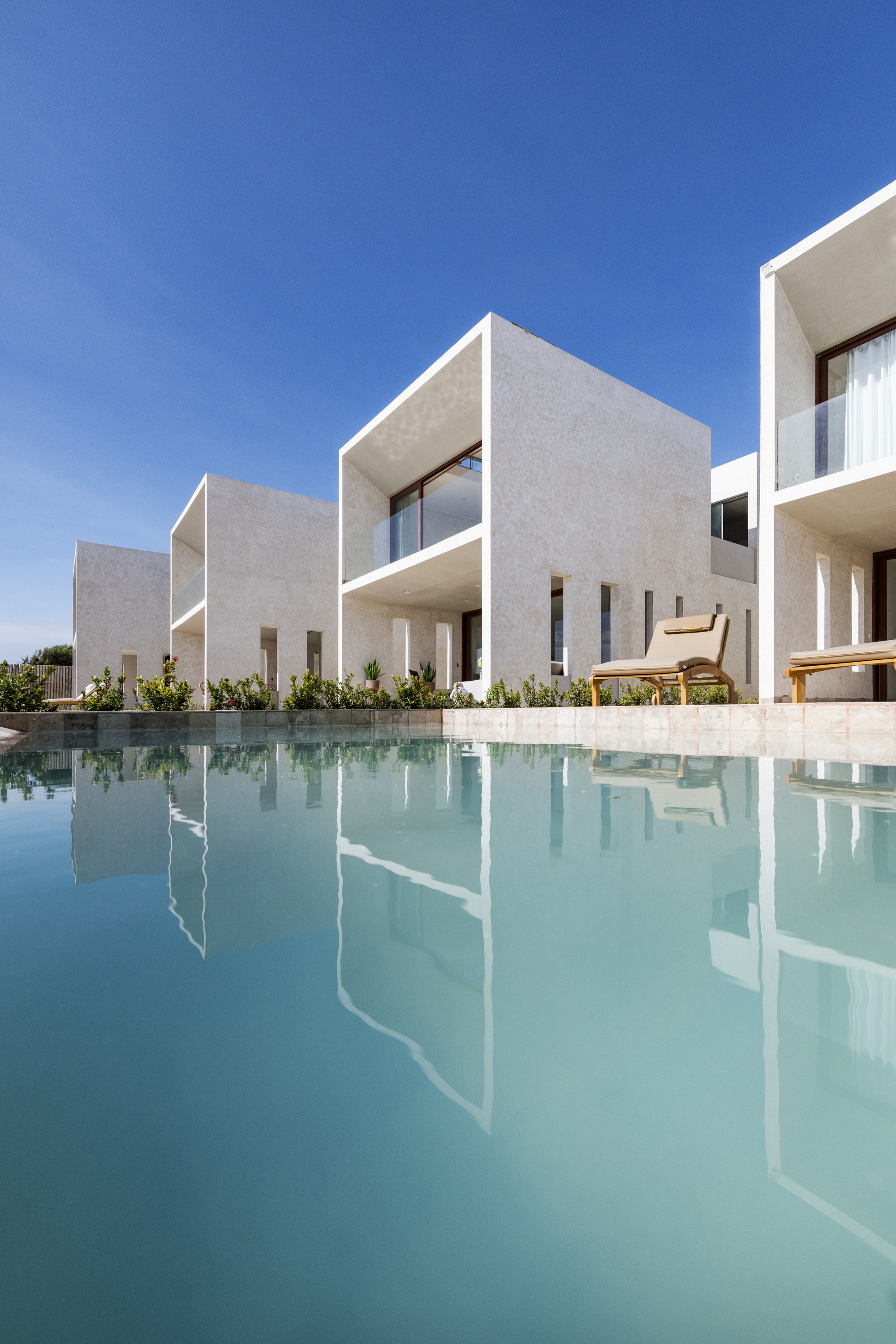 White cubic volumes reflected in a still rectangular pool under clear blue sky