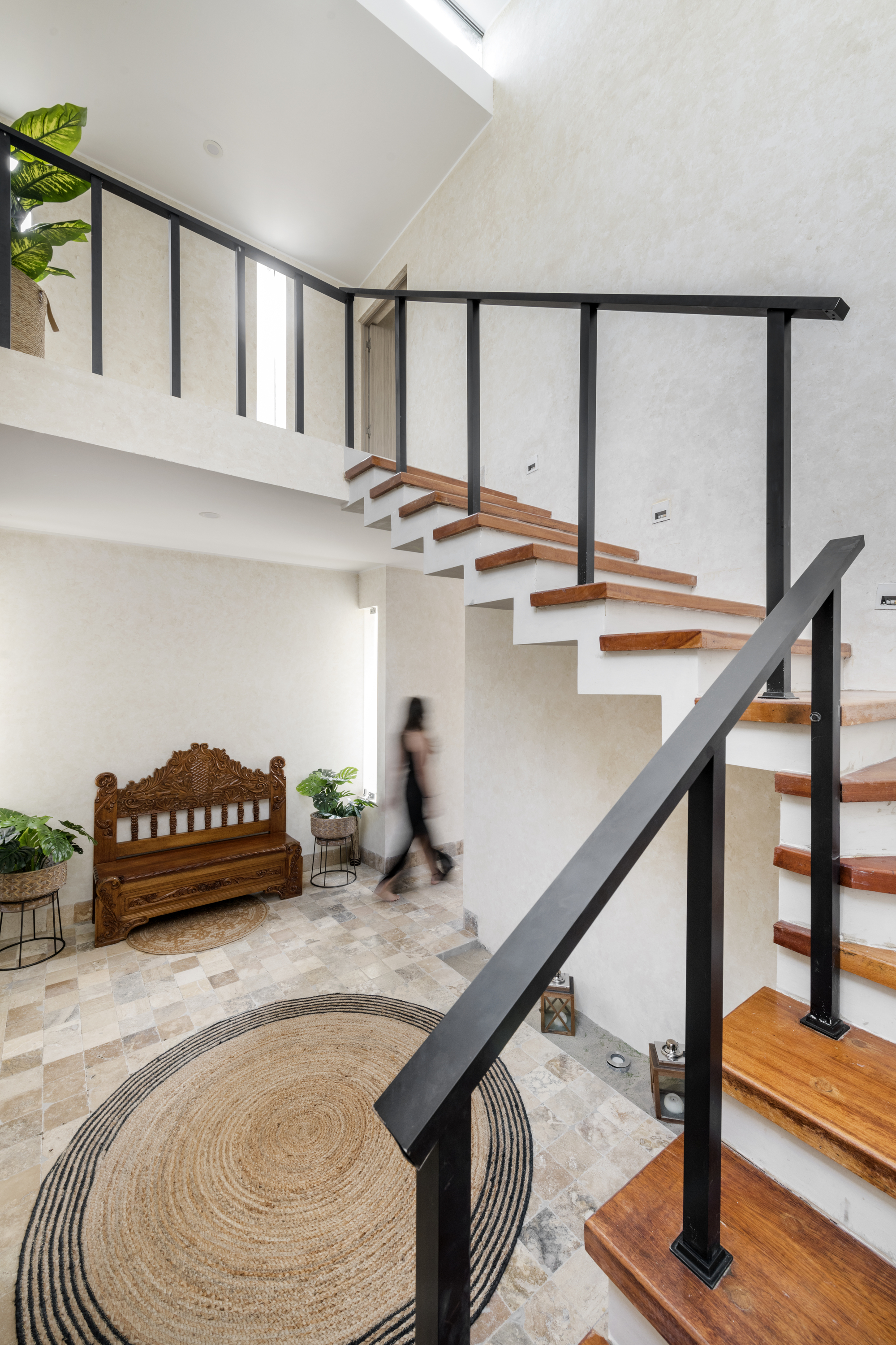 Open-tread staircase with timber treads and black steel railings above a double-height entry hall