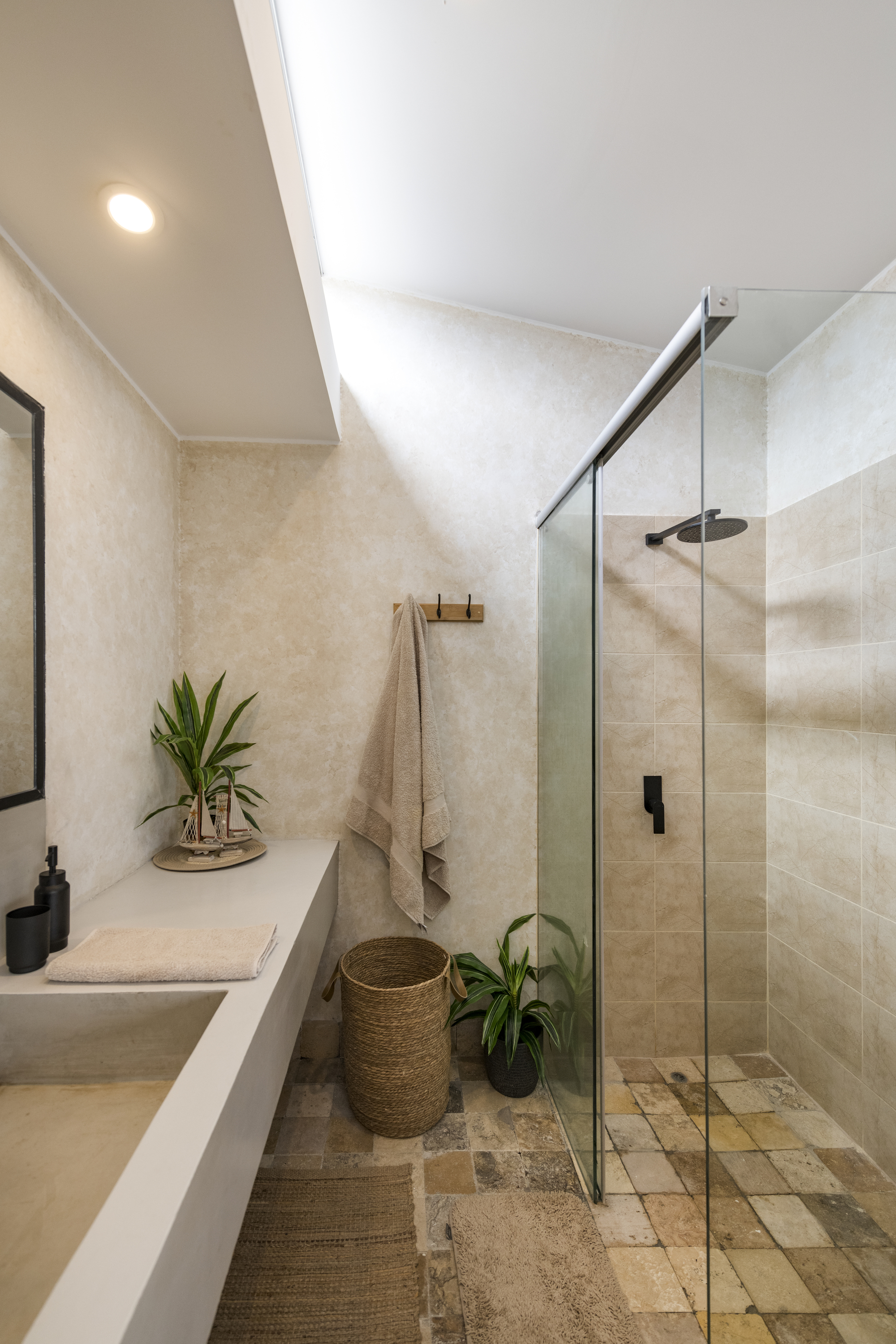 Bathroom with walk-in glass shower enclosure and skylight above a cast concrete vanity