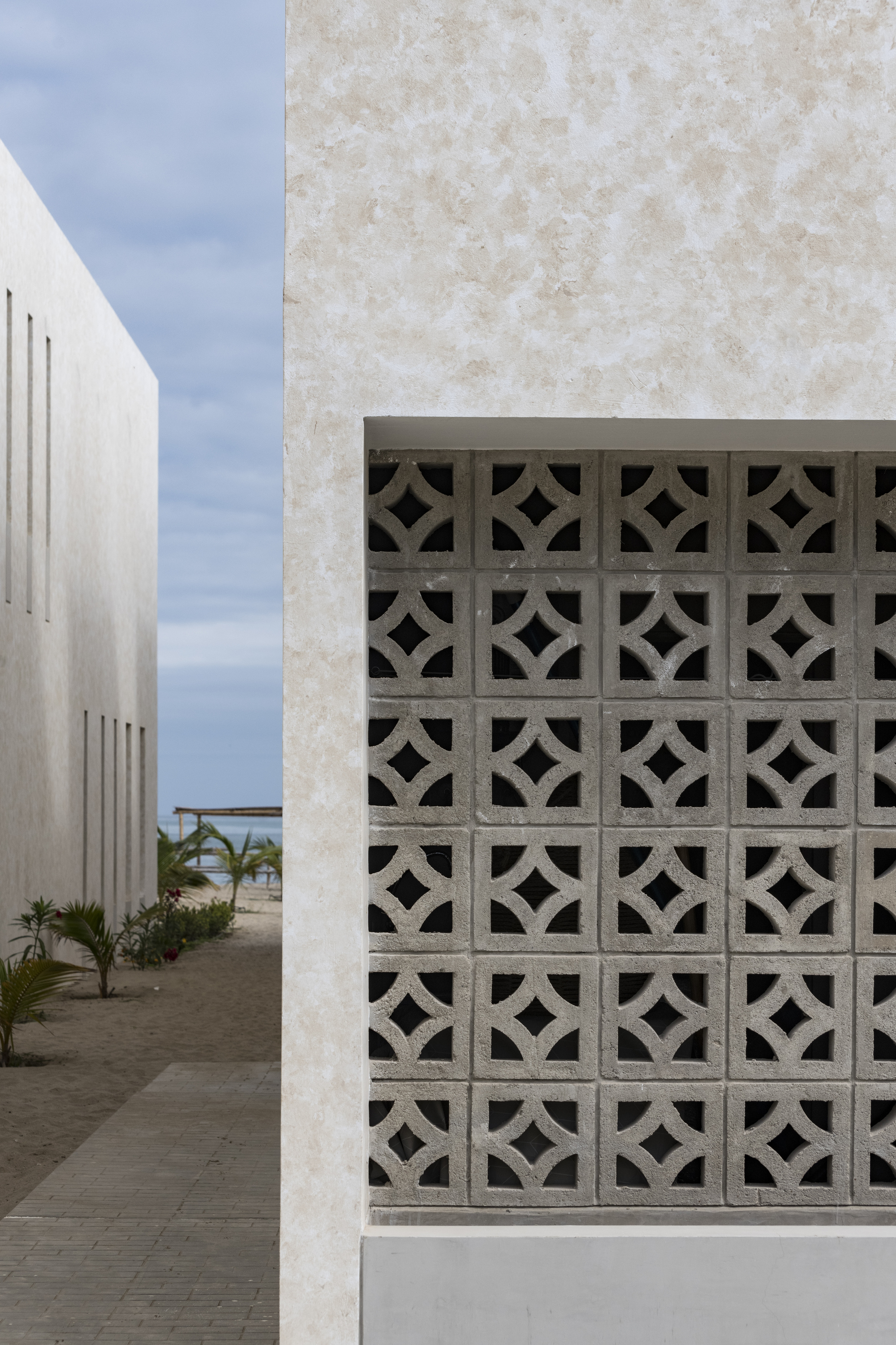 Courtyard view with geometric breeze block screen set within a pale stucco facade under soft clouds