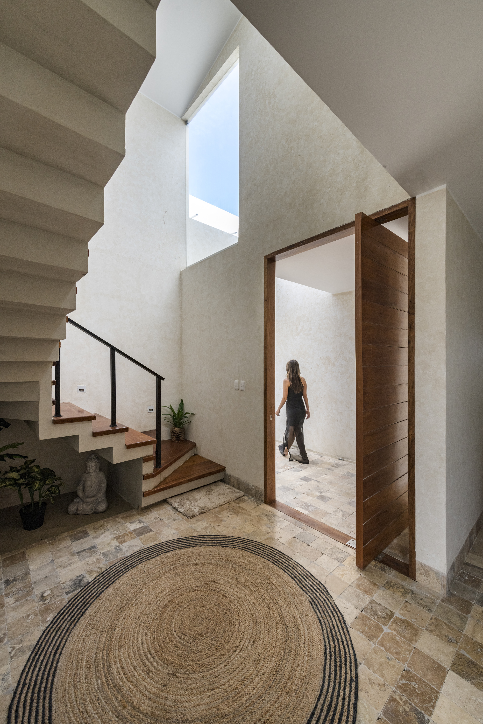 Entry hall with cantilevered staircase, skylight, timber pivot door and a woman passing through