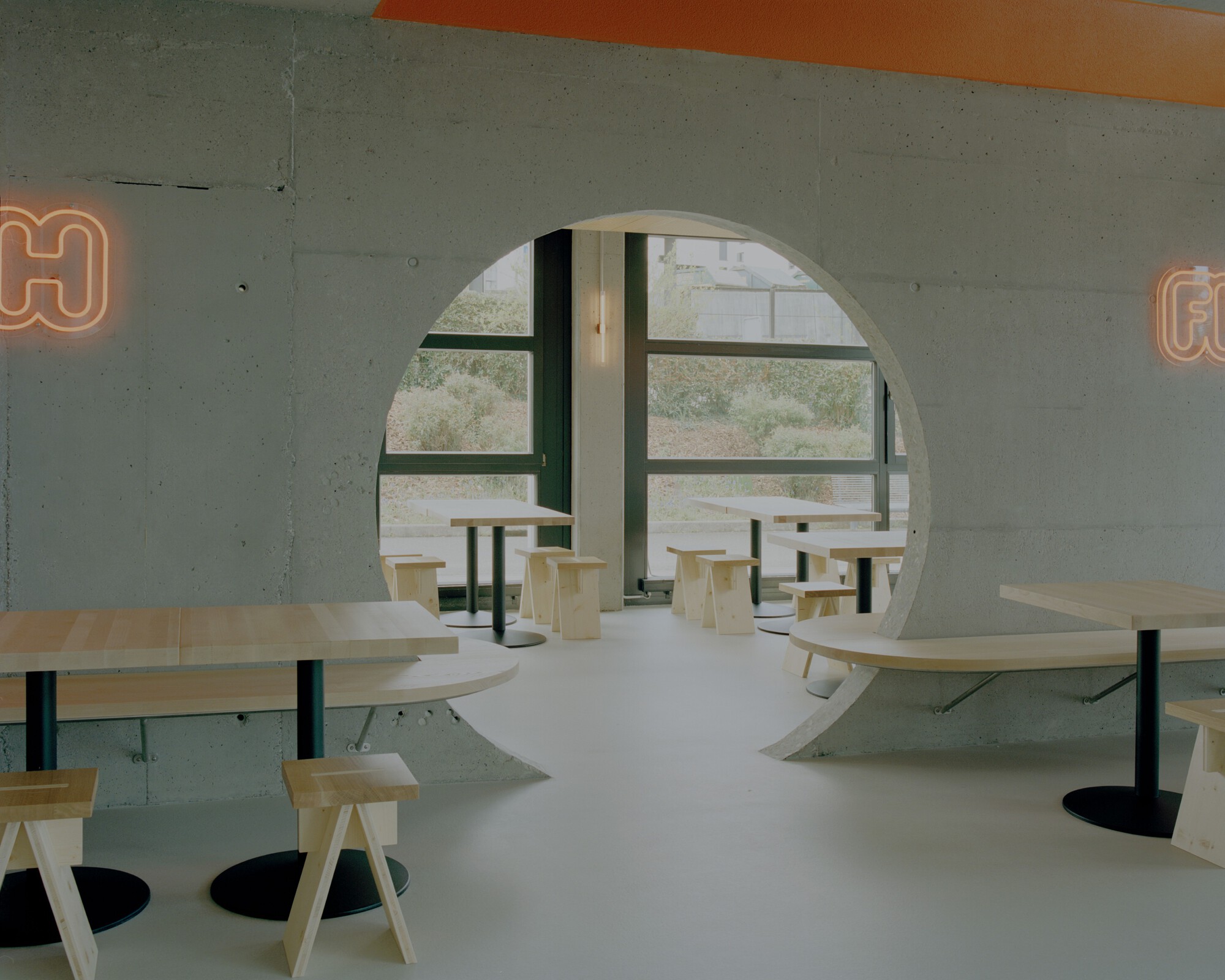 Round opening in a concrete wall revealing plywood seating and windows looking out to vegetation