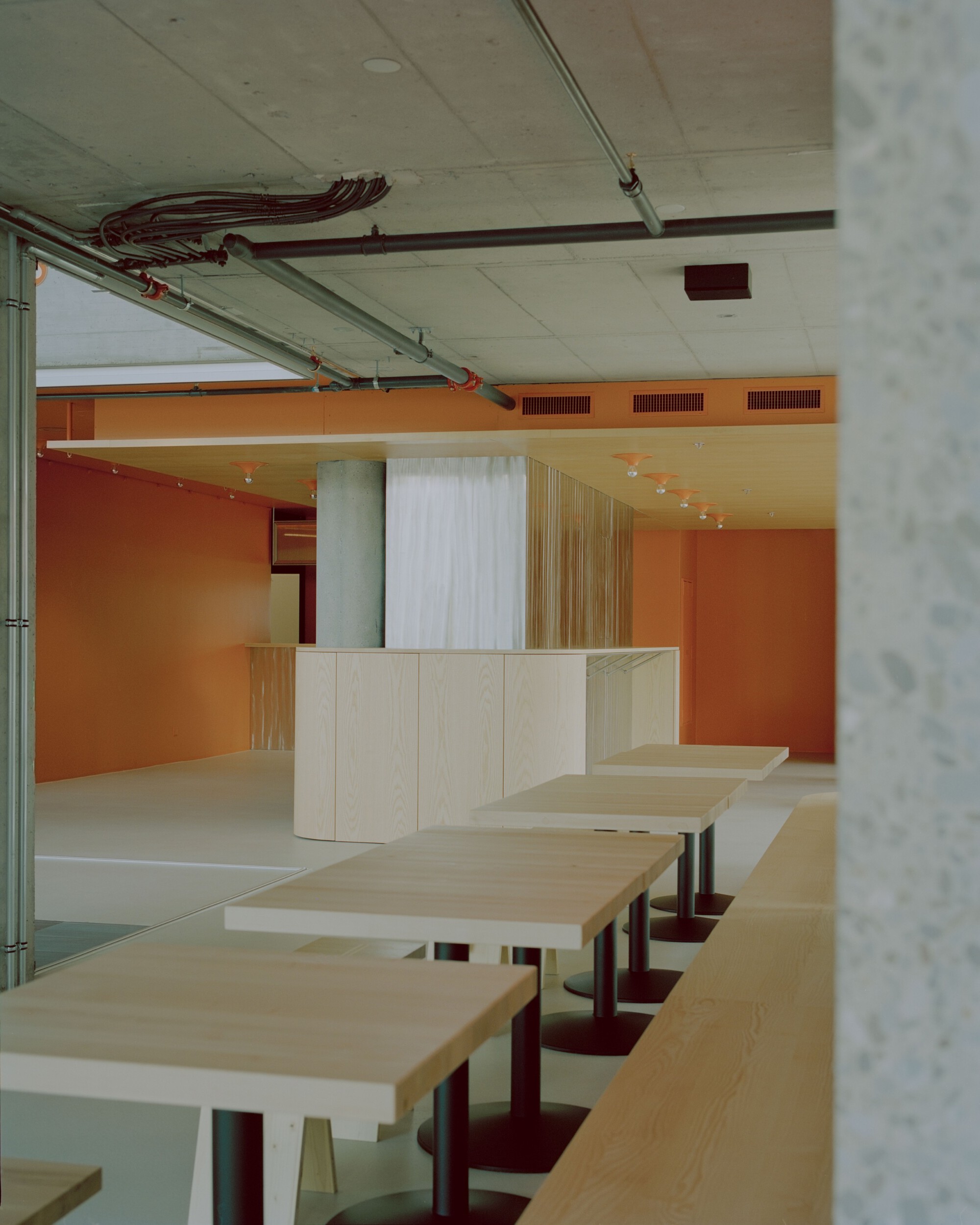 View through concrete column toward pale wood service counter and orange wall with louvered vents above