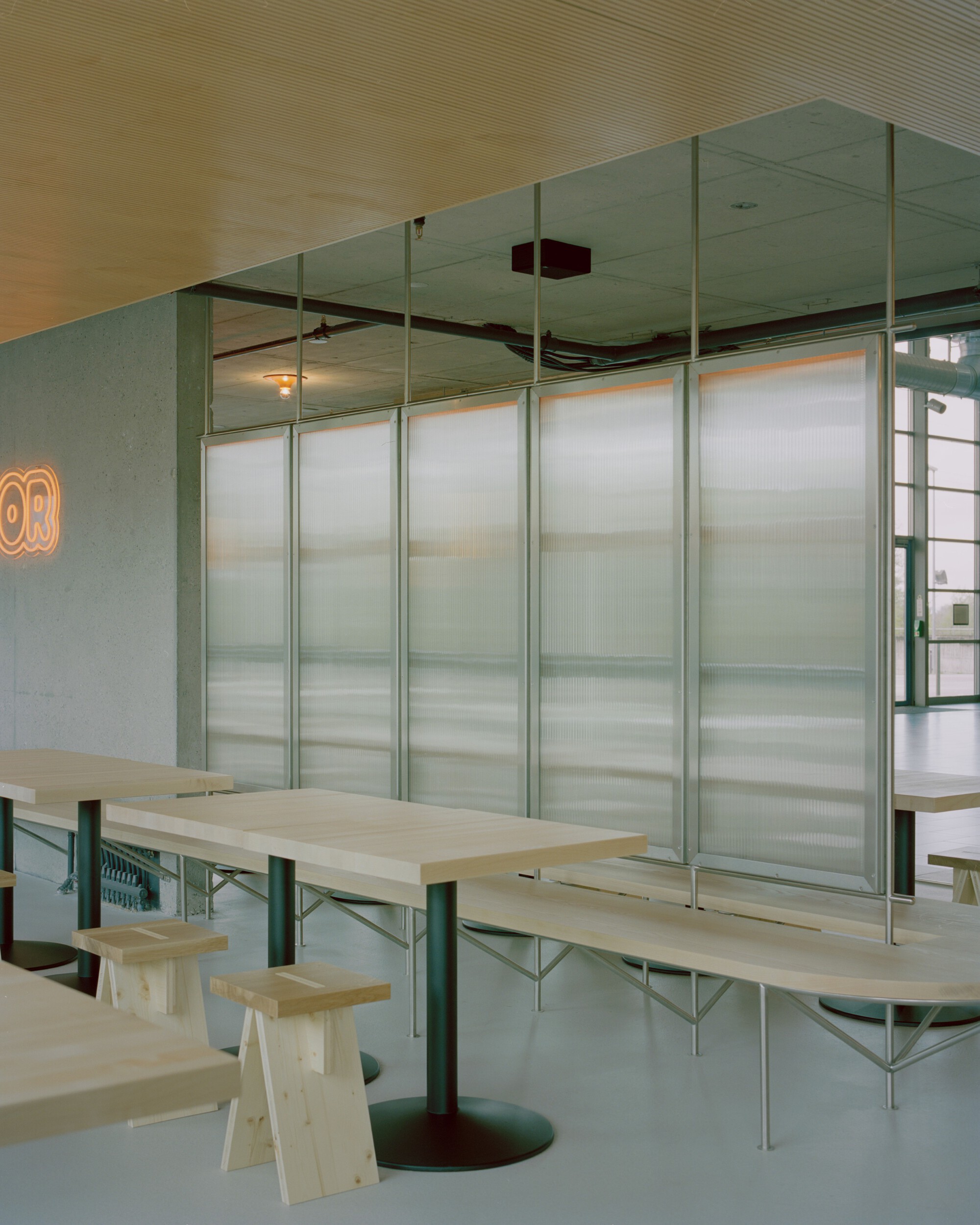 Dining area with plywood tables and translucent corrugated panel partitions on green steel frames