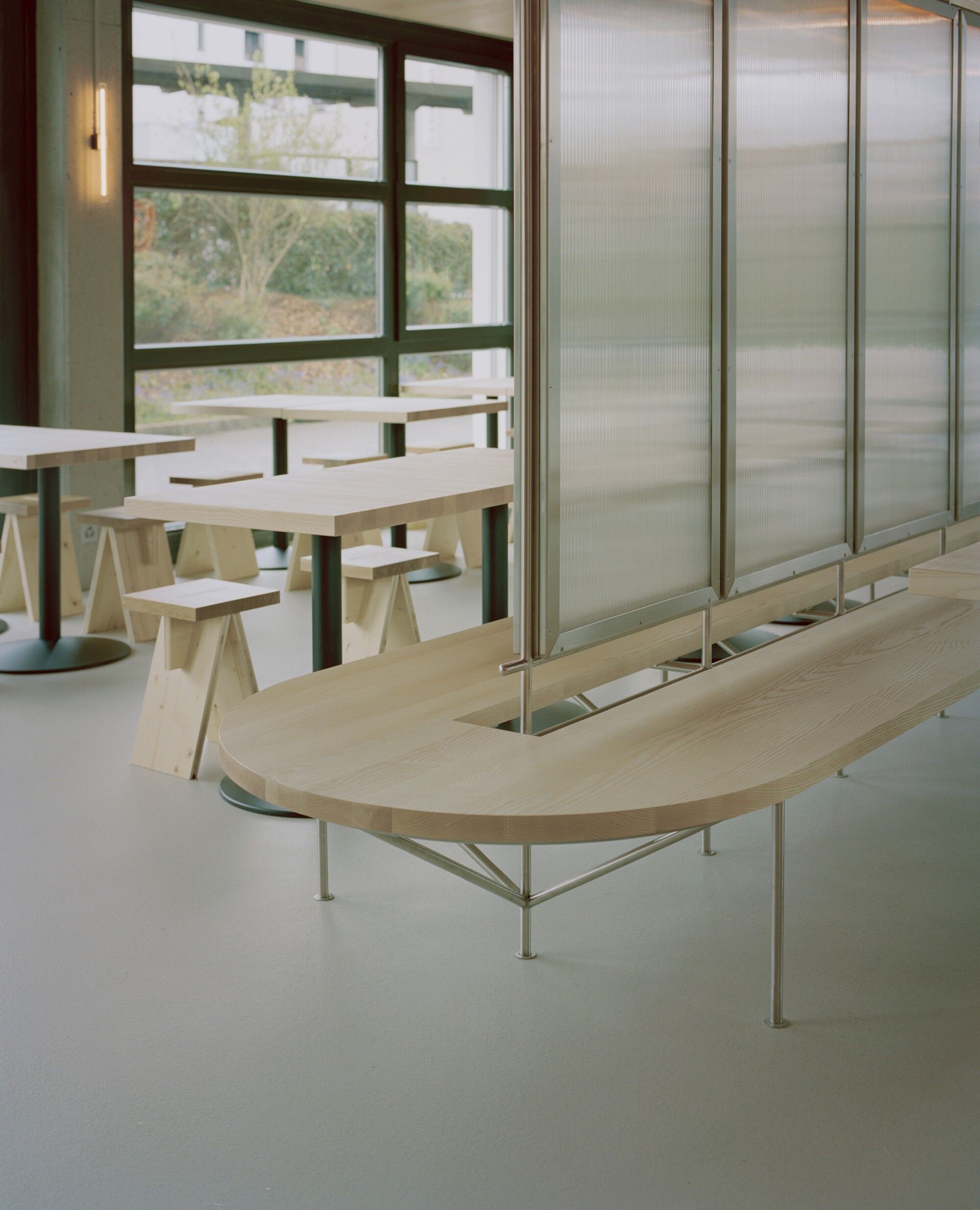 Curved plywood bench beside translucent sliding panels with view to planted greenery beyond window