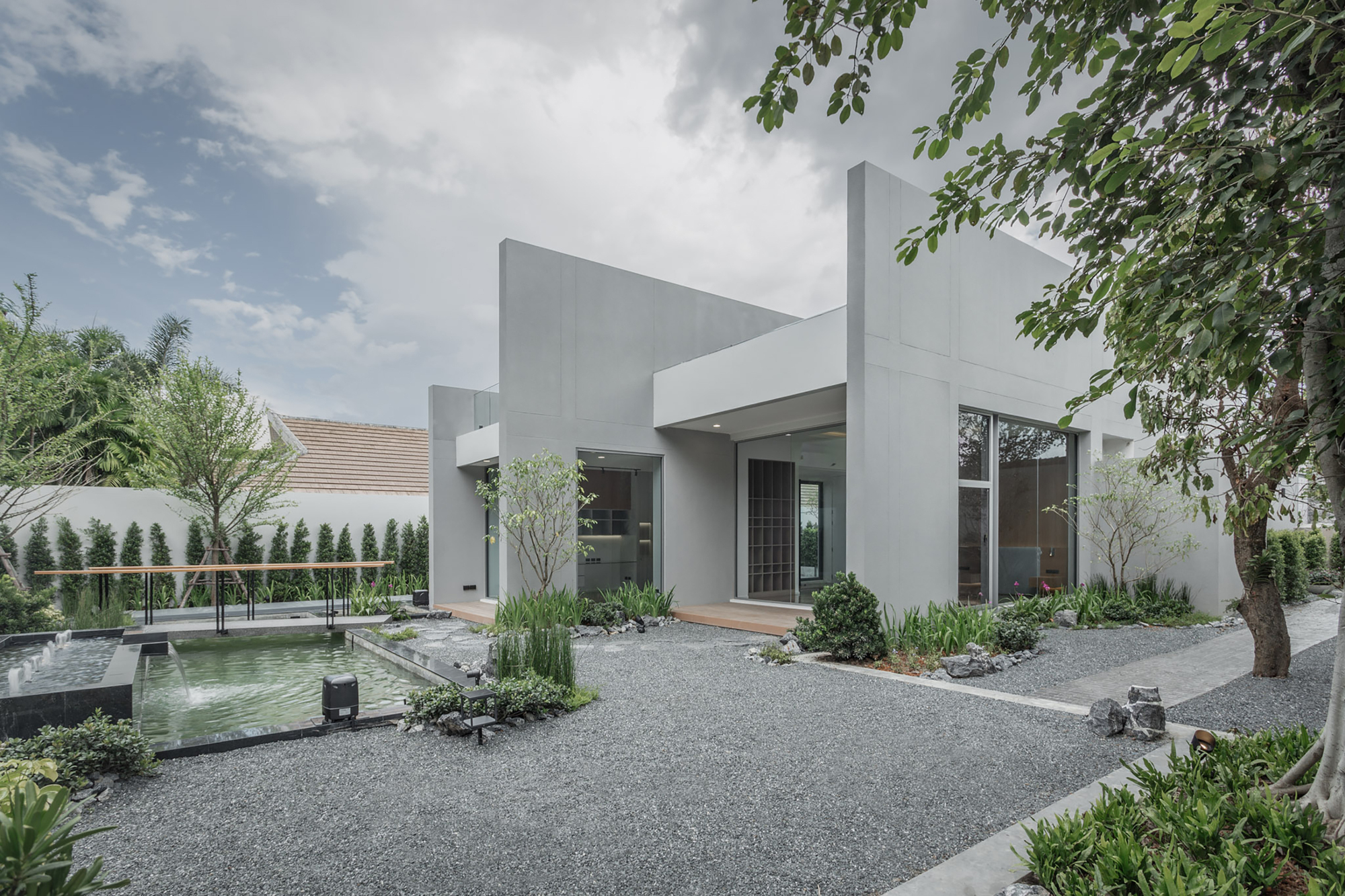 White stucco facade with recessed entry and shallow reflecting pool surrounded by gravel and planted beds