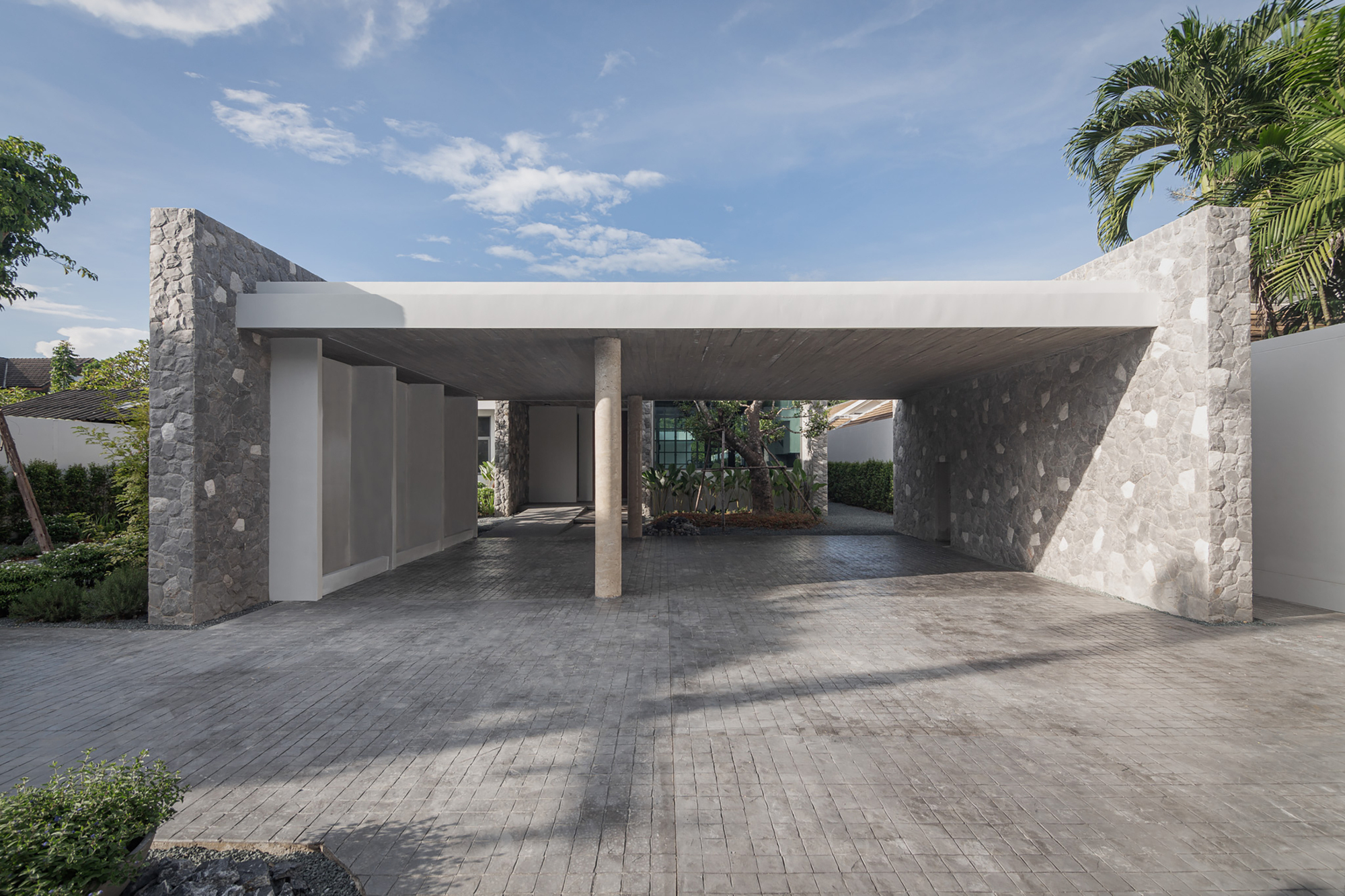 Covered carport with flat concrete canopy supported by stone-clad piers and a single round column