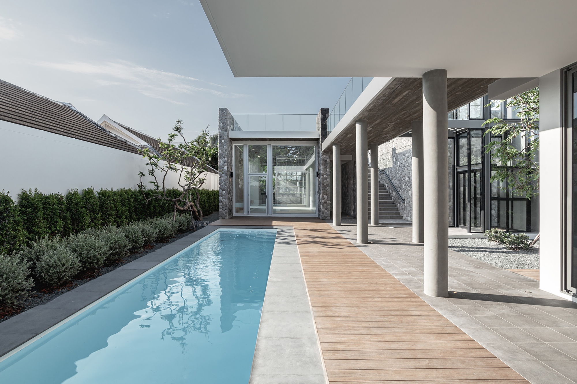 Covered terrace with white columns alongside a lap pool and timber deck opening to planted beds