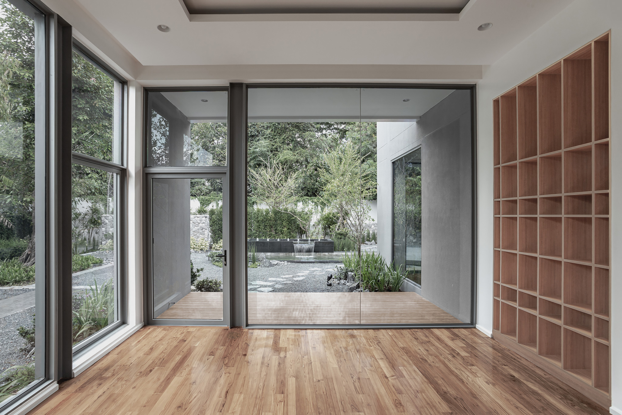 Living space with built-in timber shelving and sliding glass doors overlooking gravel courtyard garden