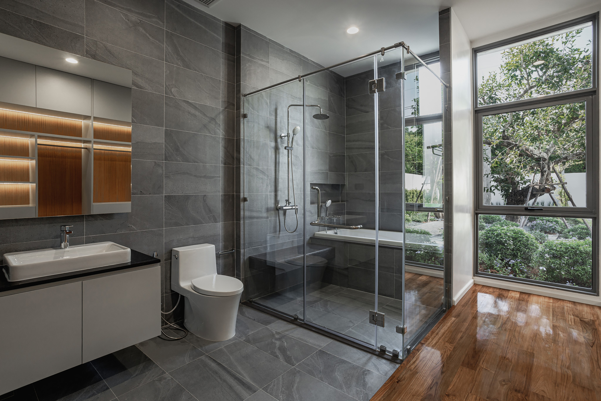 Bathroom with glass-enclosed shower and large window framing views of garden and trees outside