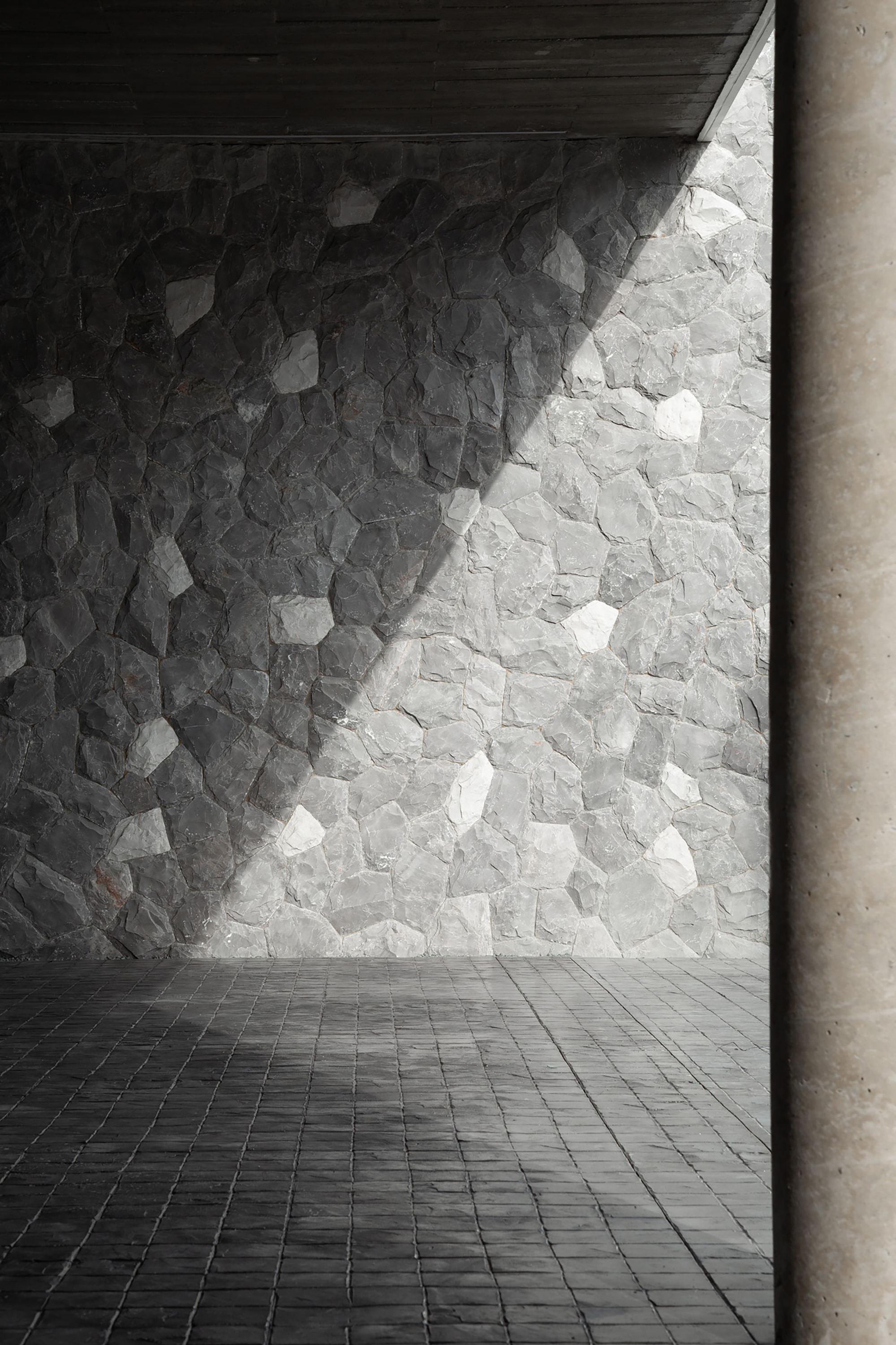 Stone-clad wall with irregular pieces in light and shadow next to a concrete column