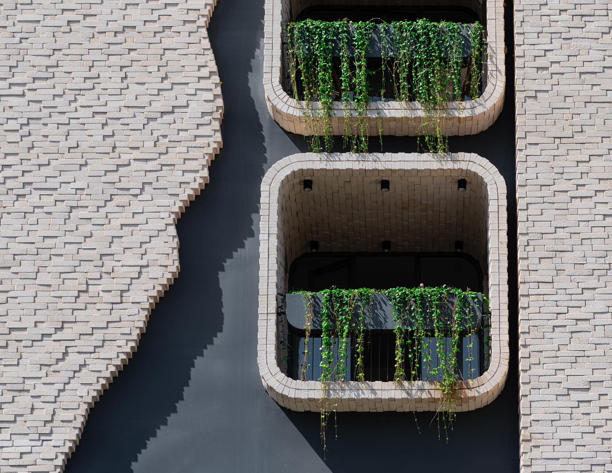 Overhead view of two stacked balconies with rounded brick frames and trailing vines