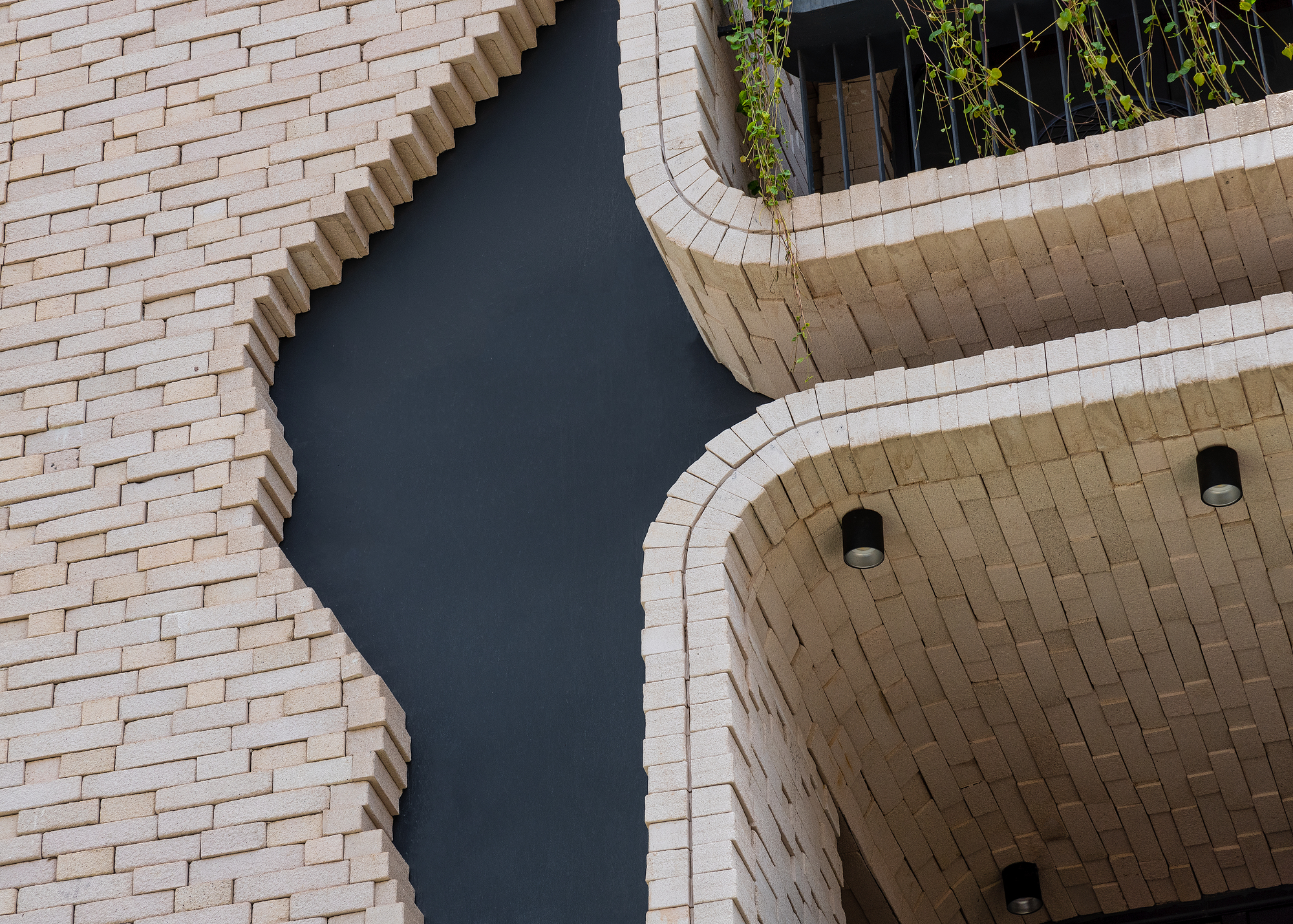 Upward view of curved brick soffits and recessed downlights meeting textured masonry wall