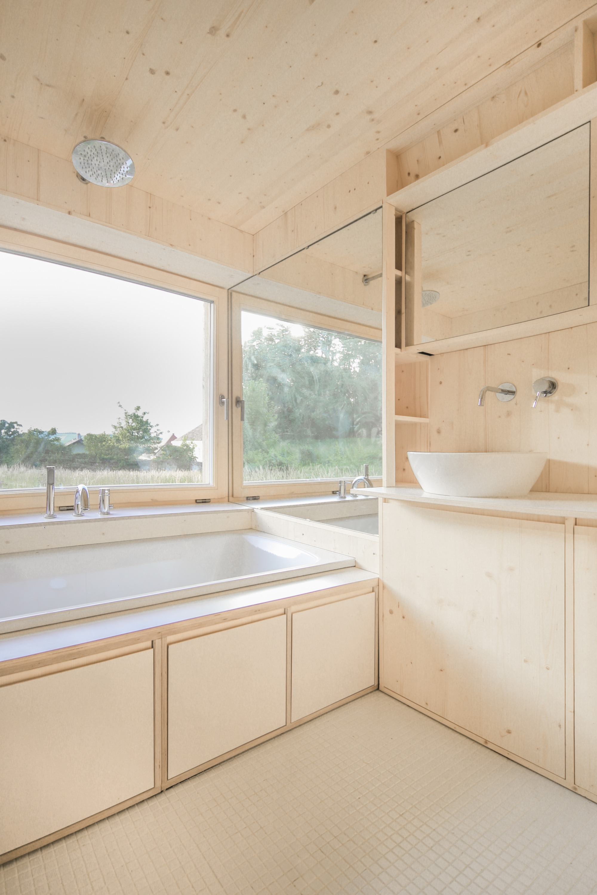 Pale plywood bathroom interior with built-in tub and basin beneath a sloped ceiling
