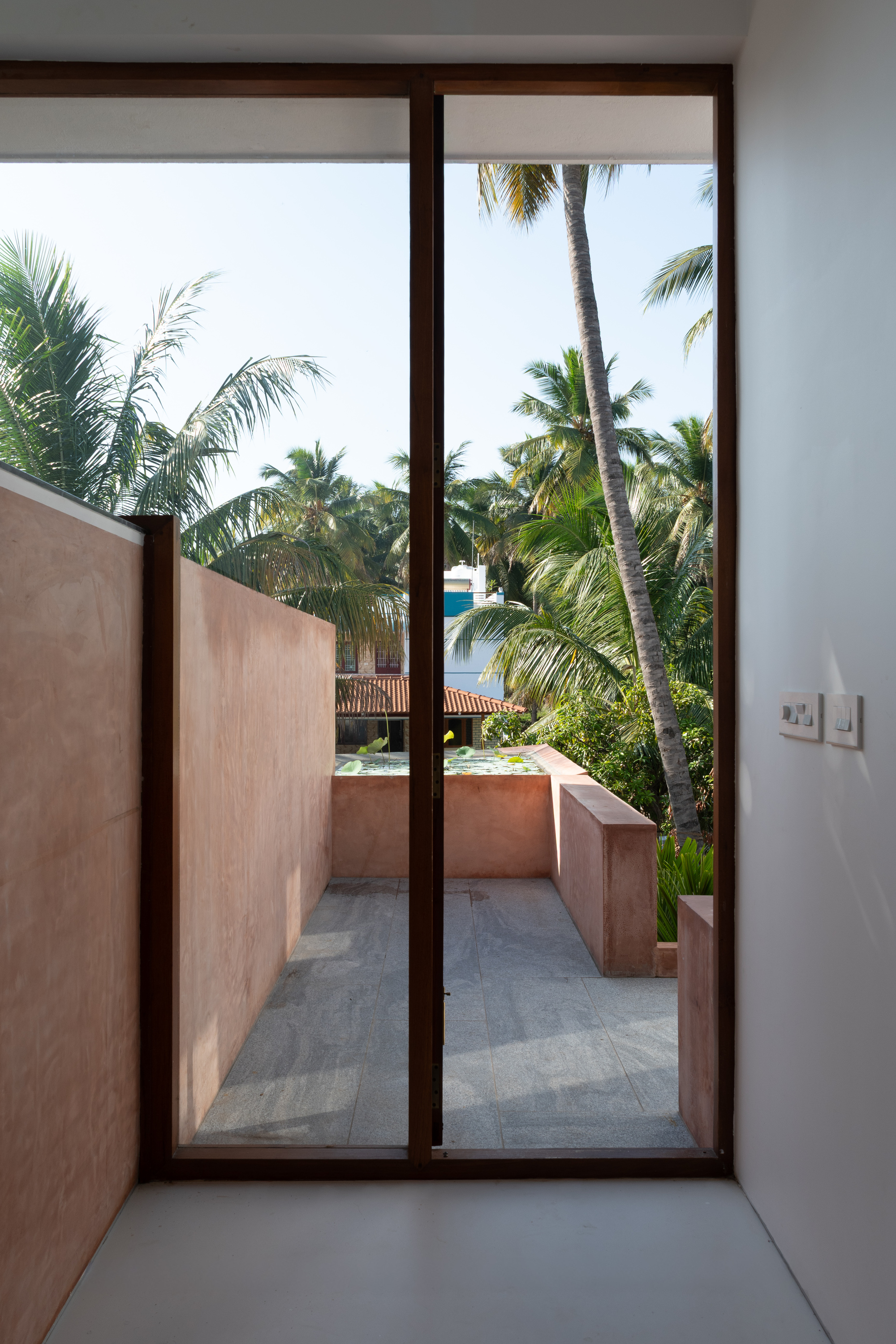 Tall glazed door framing a pink-walled courtyard with palm trees beyond