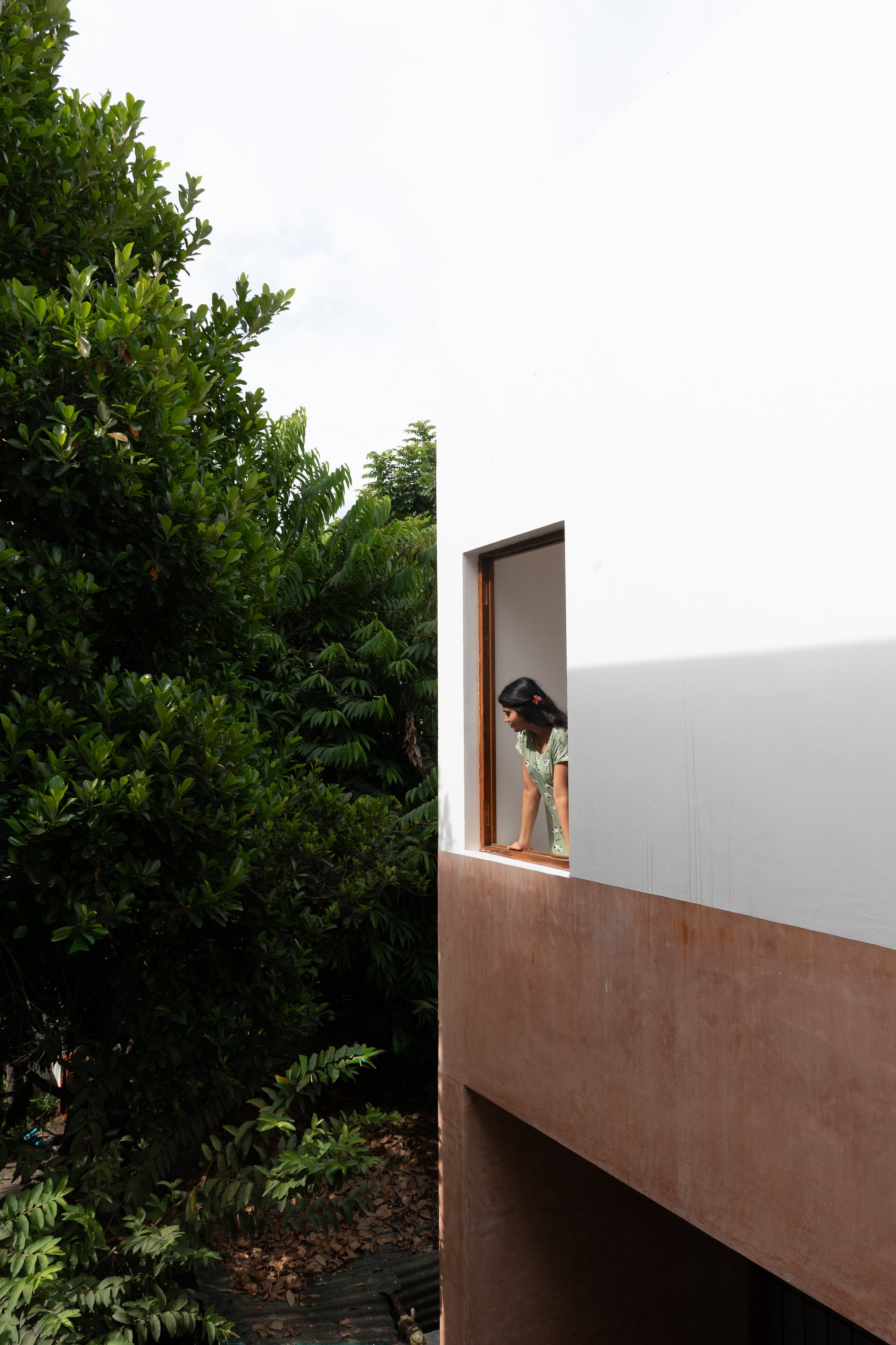 Cantilevered balcony with wood base and white parapet where a person stands beside foliage