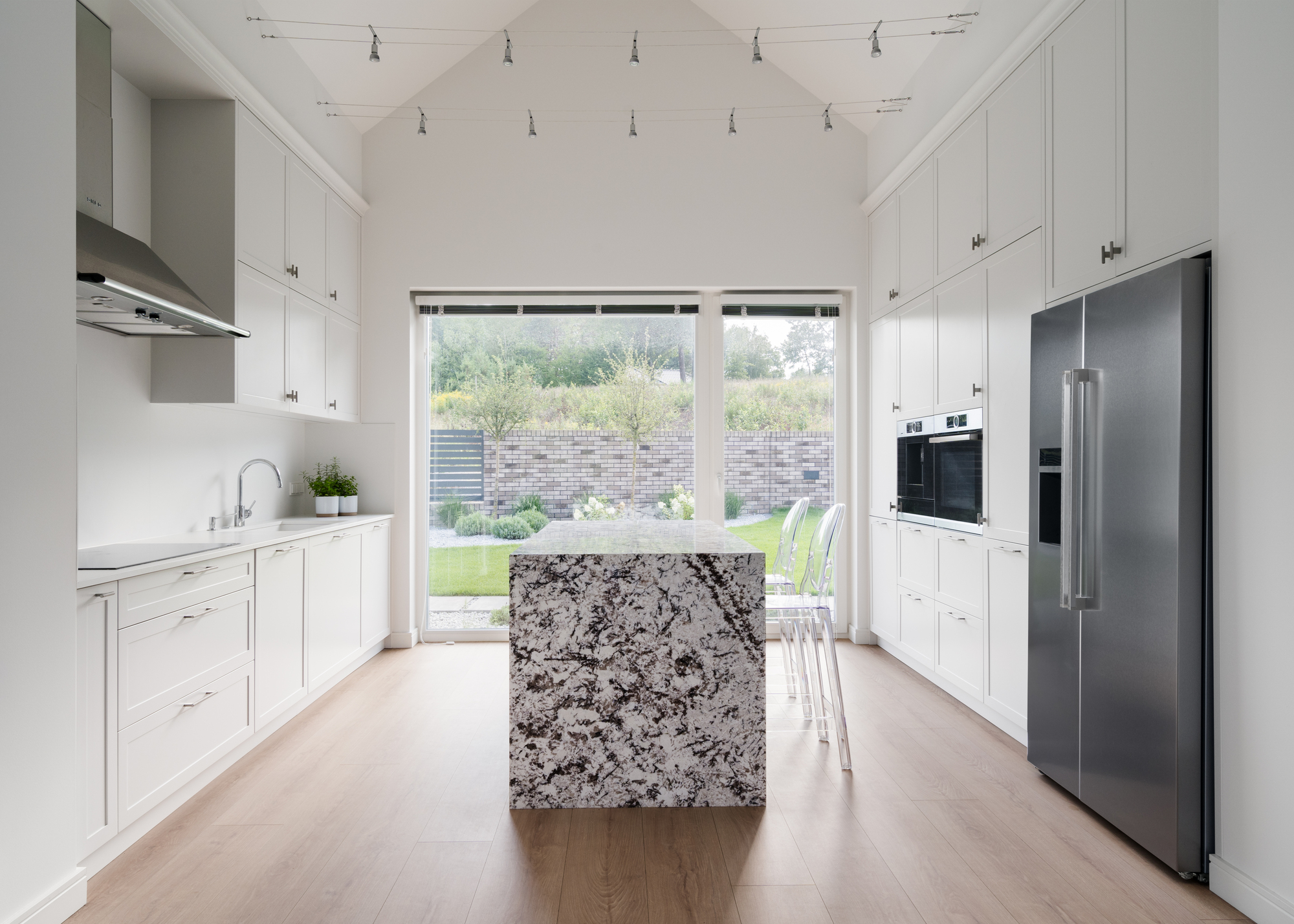 White galley kitchen with granite island, track lighting, and glass doors opening to the lawn beyond