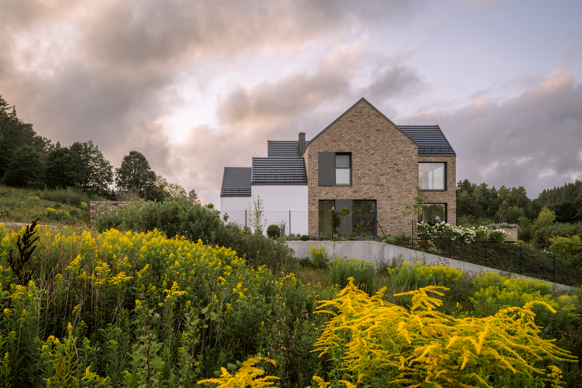 Brick and render gable facade rising above a garden of yellow flowering perennials under overcast skies