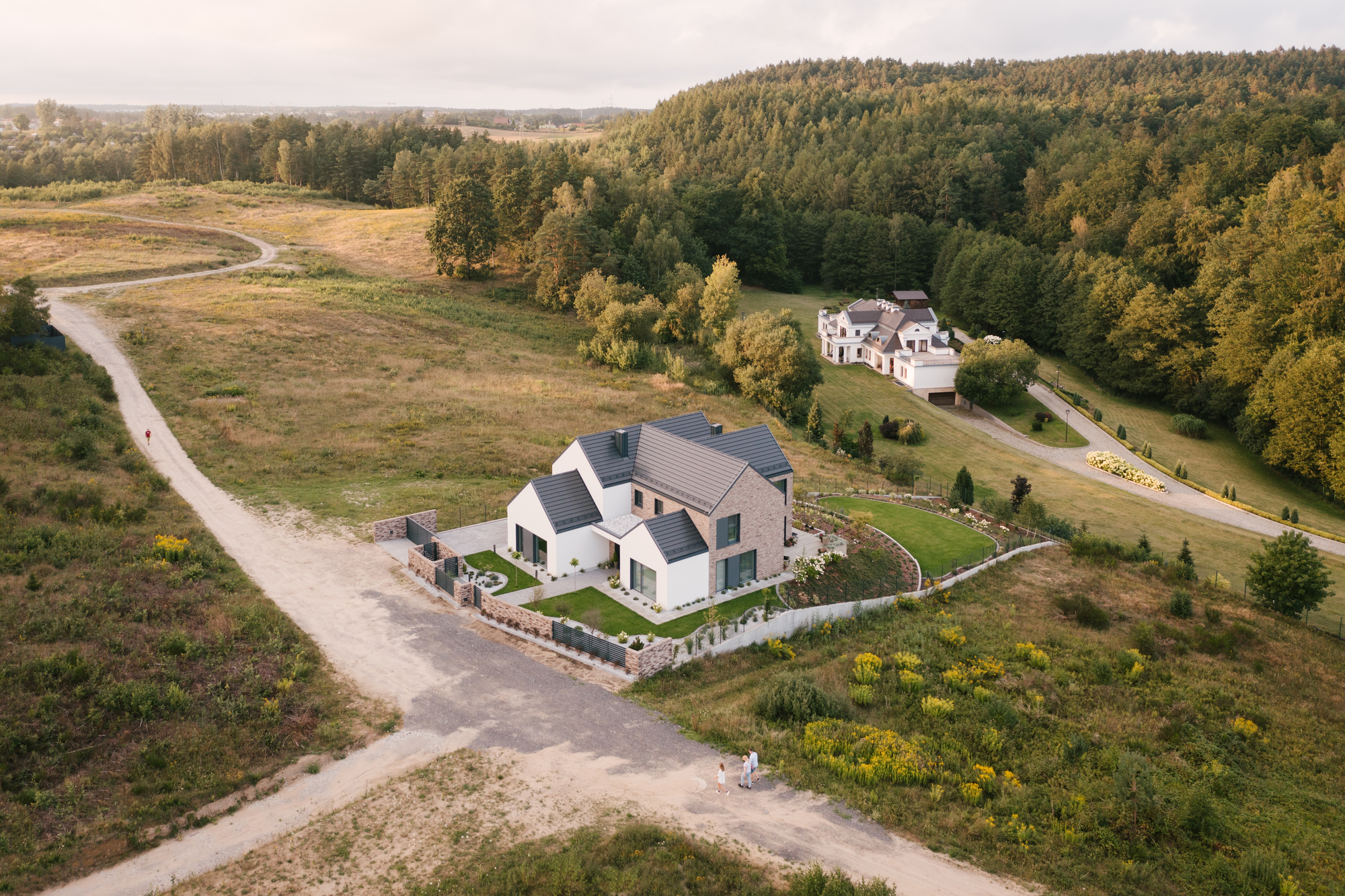 Aerial view of the gabled residence with terraced gardens surrounded by fields and forest