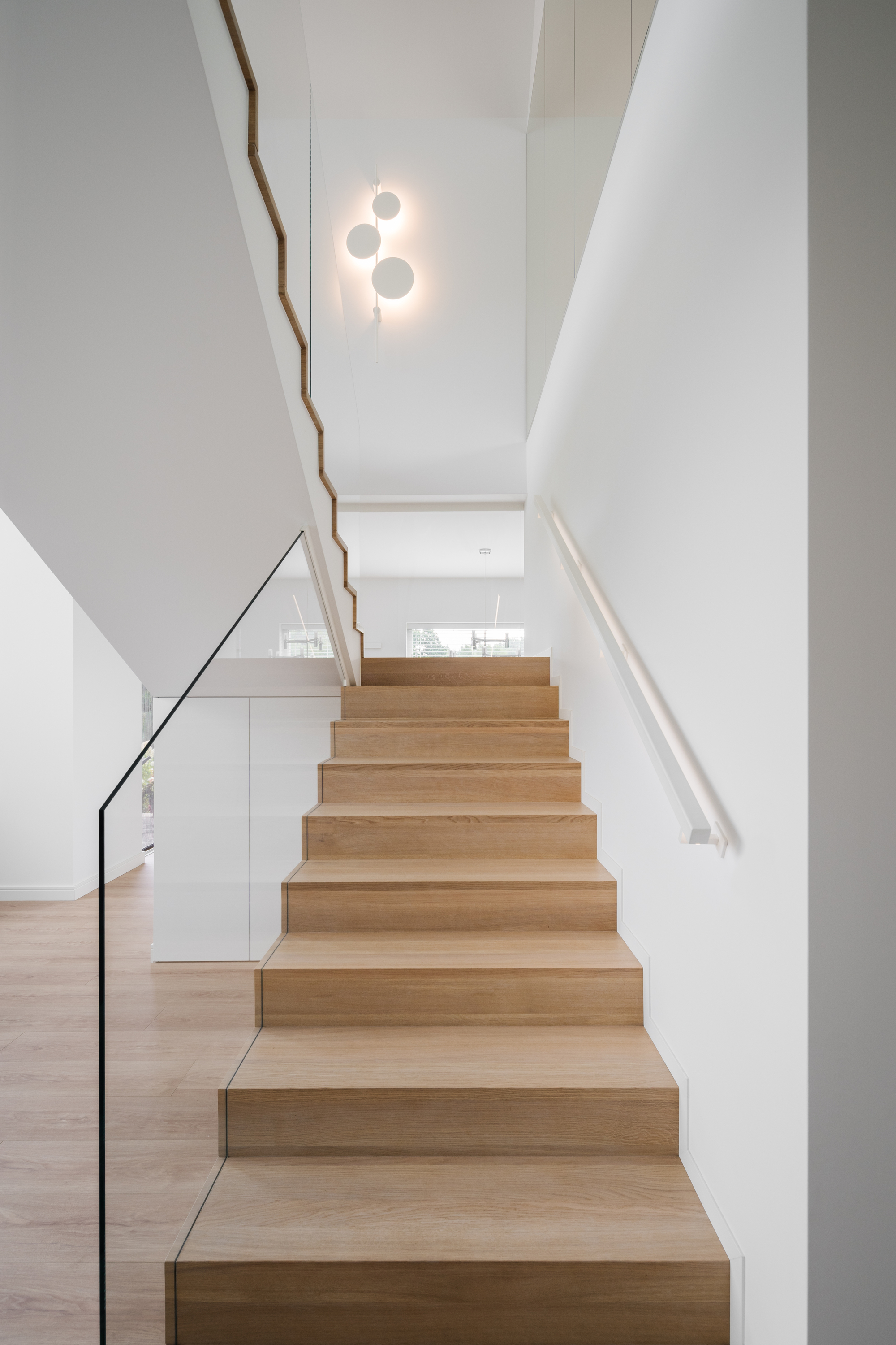 Light timber staircase with thin steel handrail and white walls beneath a circular pendant fixture