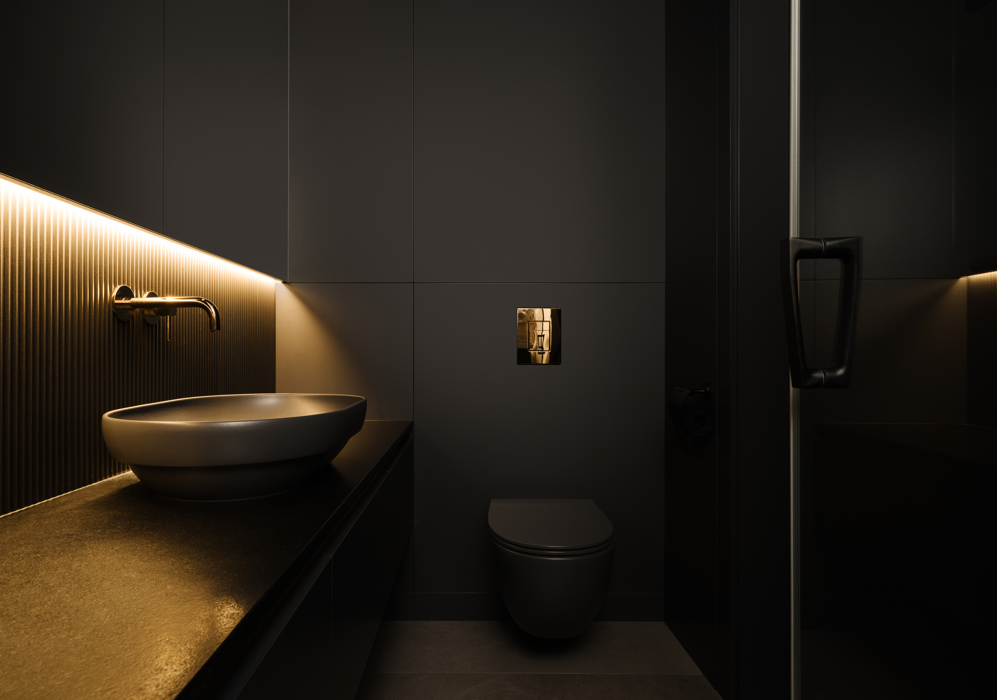 Bathroom with fluted black wall panels, integrated strip lighting, and oval vessel sink on cantilevered counter