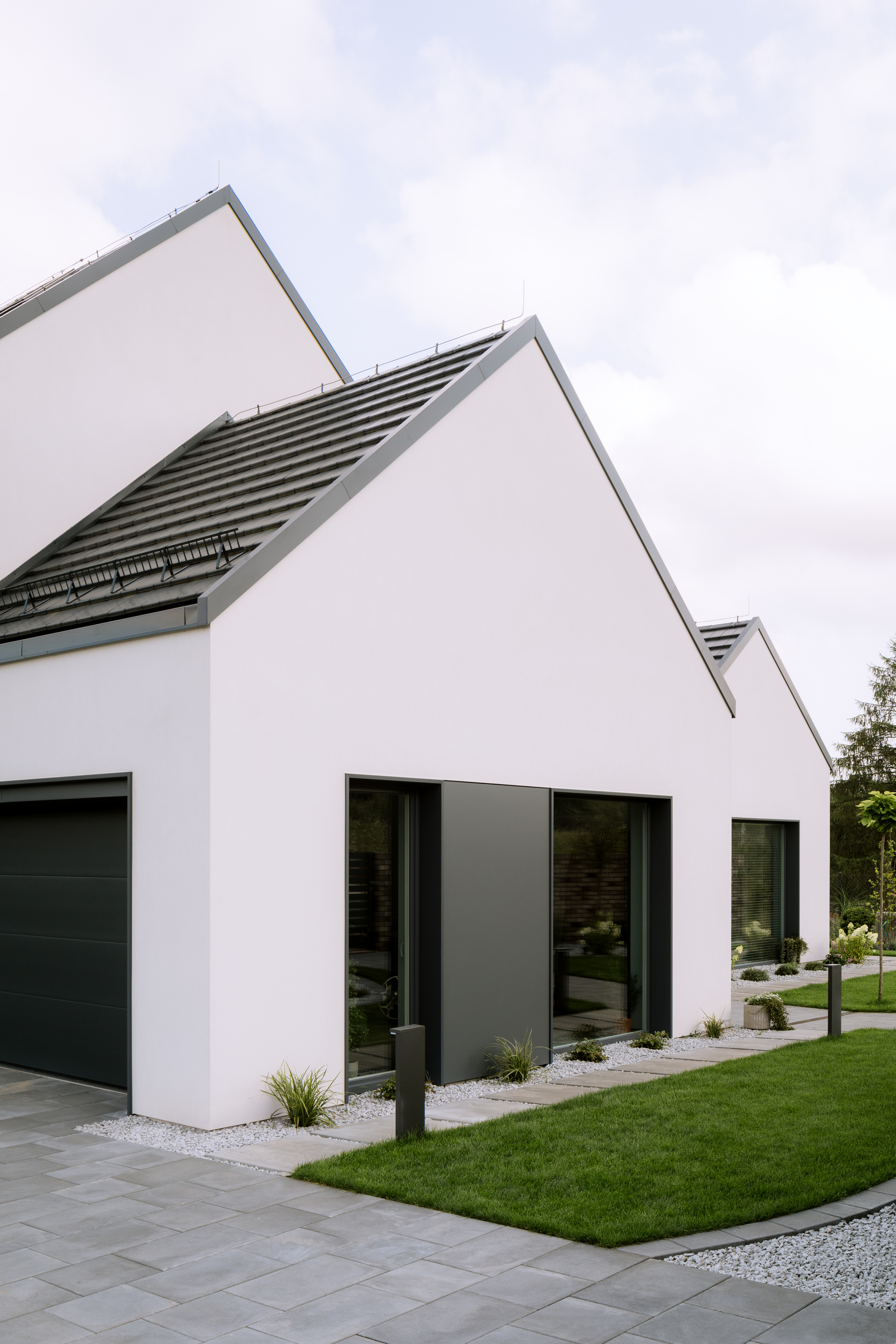 White gabled volumes with horizontal louver vents and large black-framed windows under overcast sky