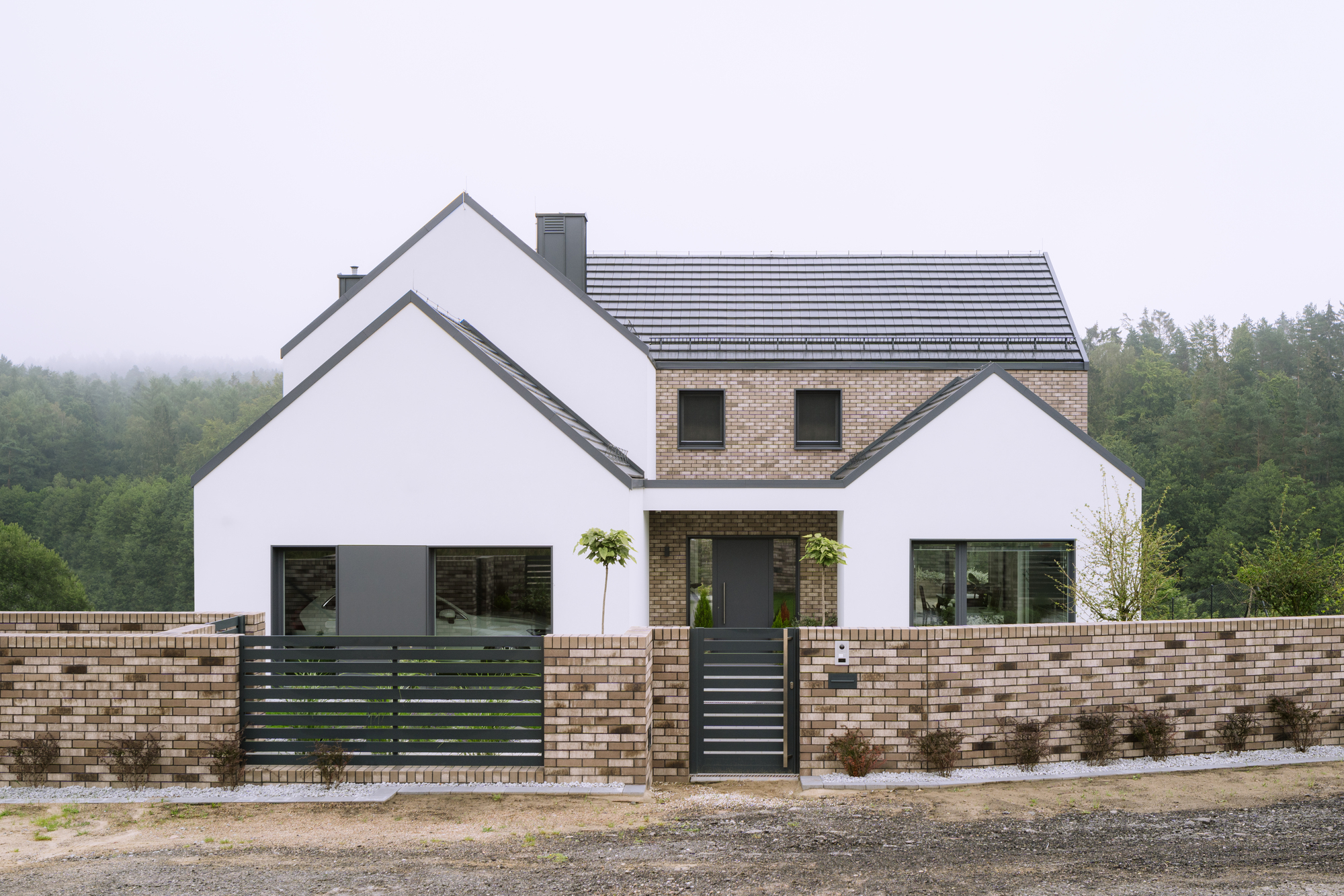 Front facade combining white stucco gables and brick upper story behind low variegated brick garden wall