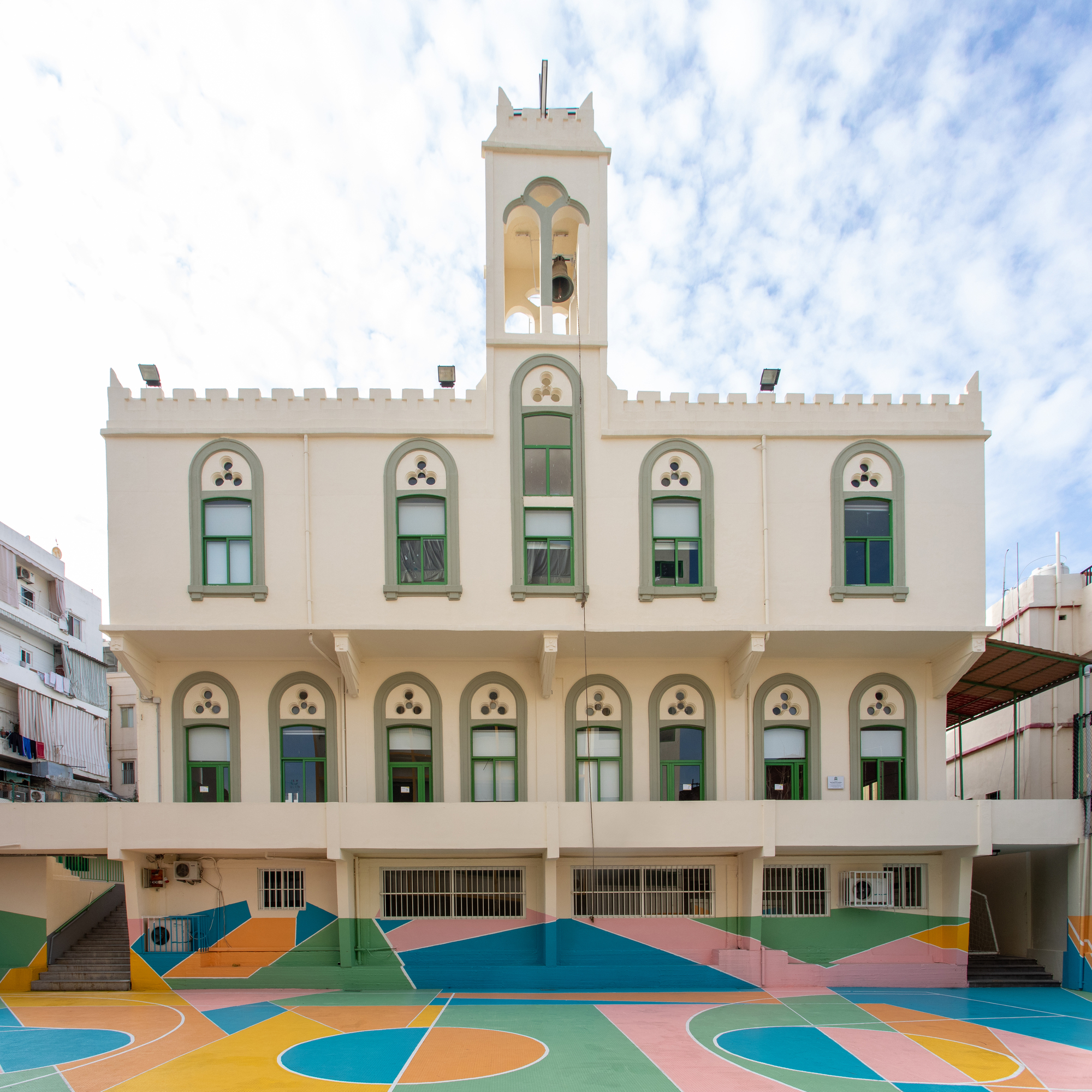 White stucco facade with arched windows and bell tower above a multicolored geometric courtyard