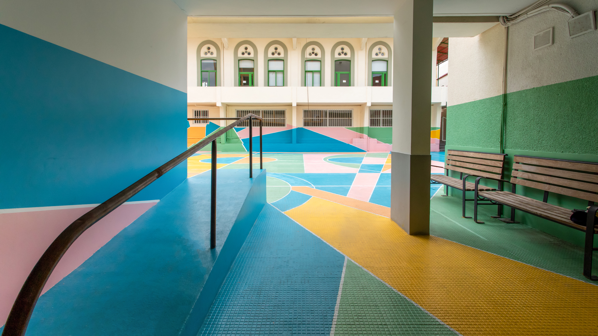 Covered walkway with steel columns overlooking the painted courtyard through arched openings