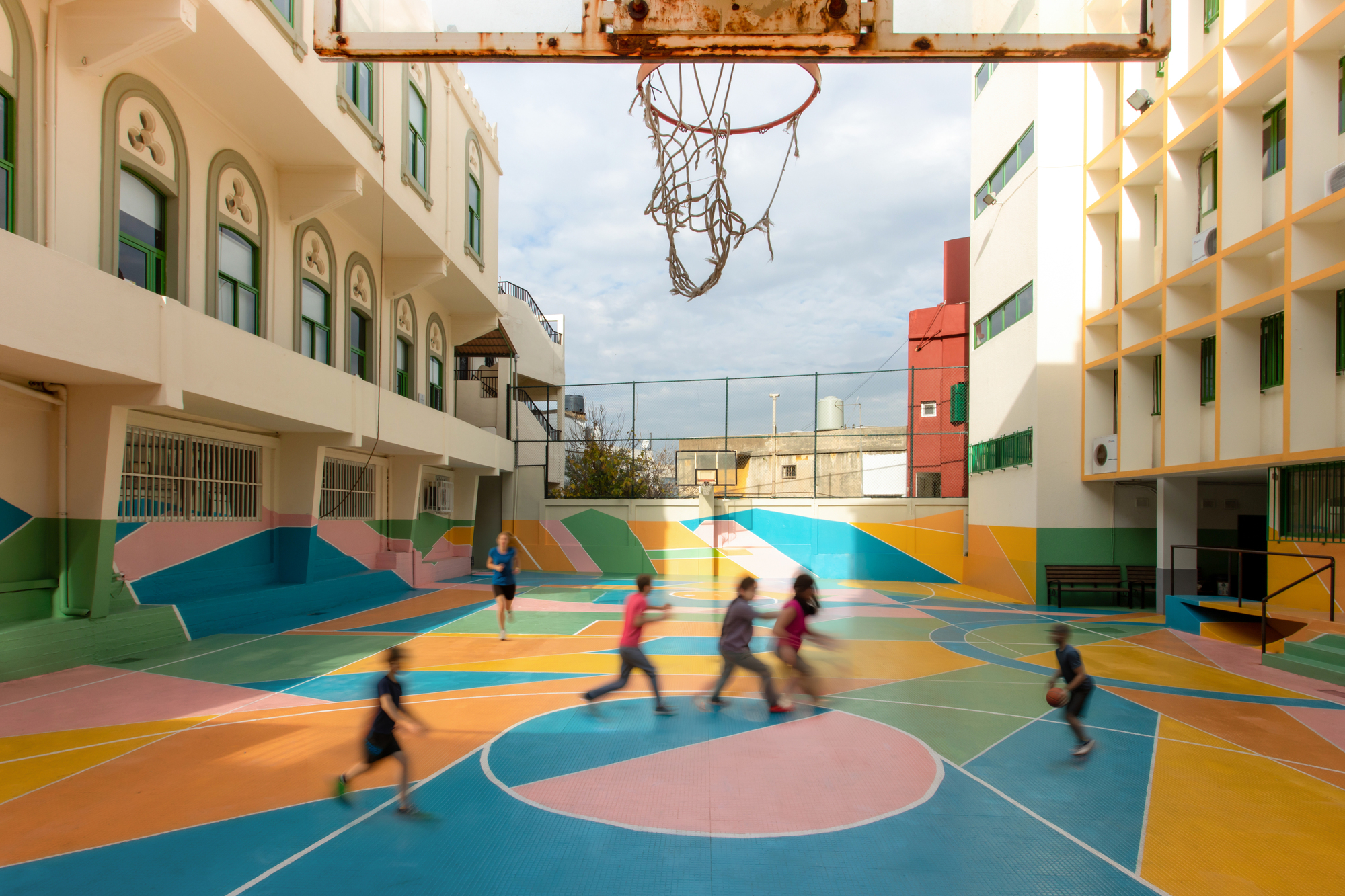 Weathered basketball hoop suspended above the painted court as children move across the surface