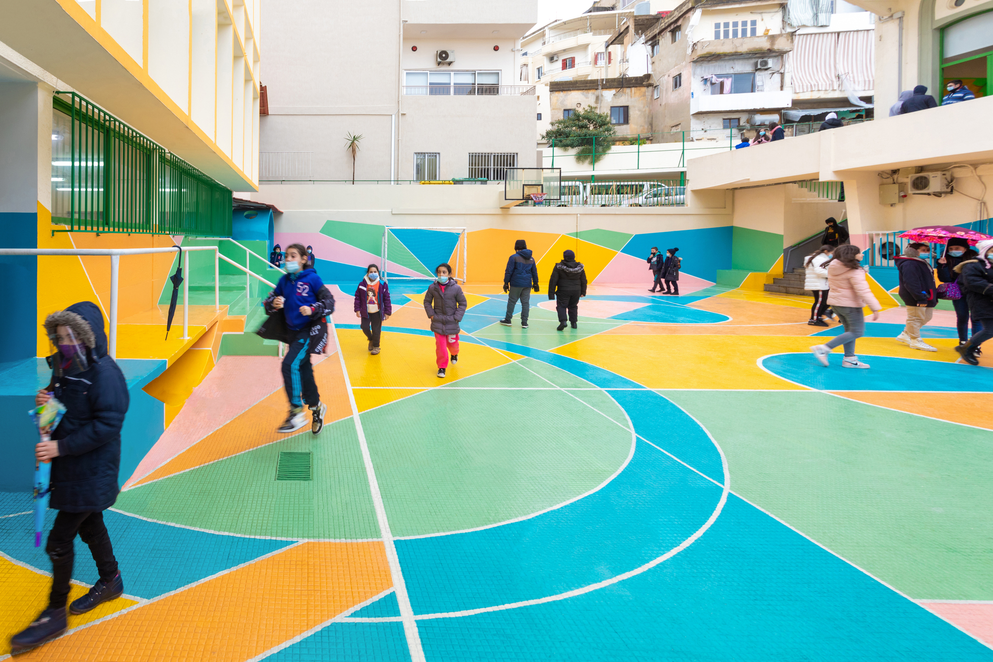 Children dispersed across the colorful court surface with surrounding residential buildings visible beyond