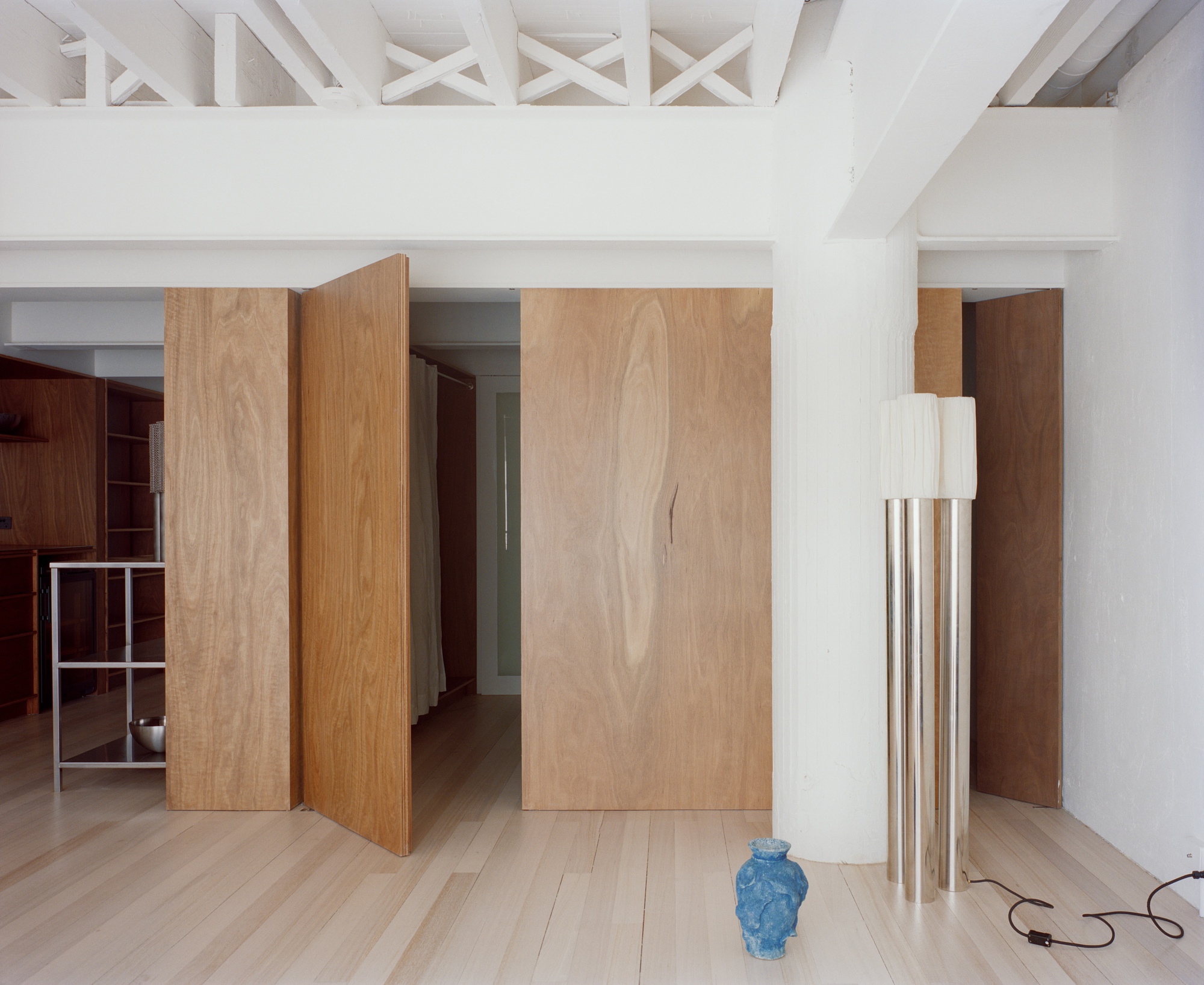 Interior with pivoting wood veneer panels and exposed white-painted roof trusses above pale timber flooring