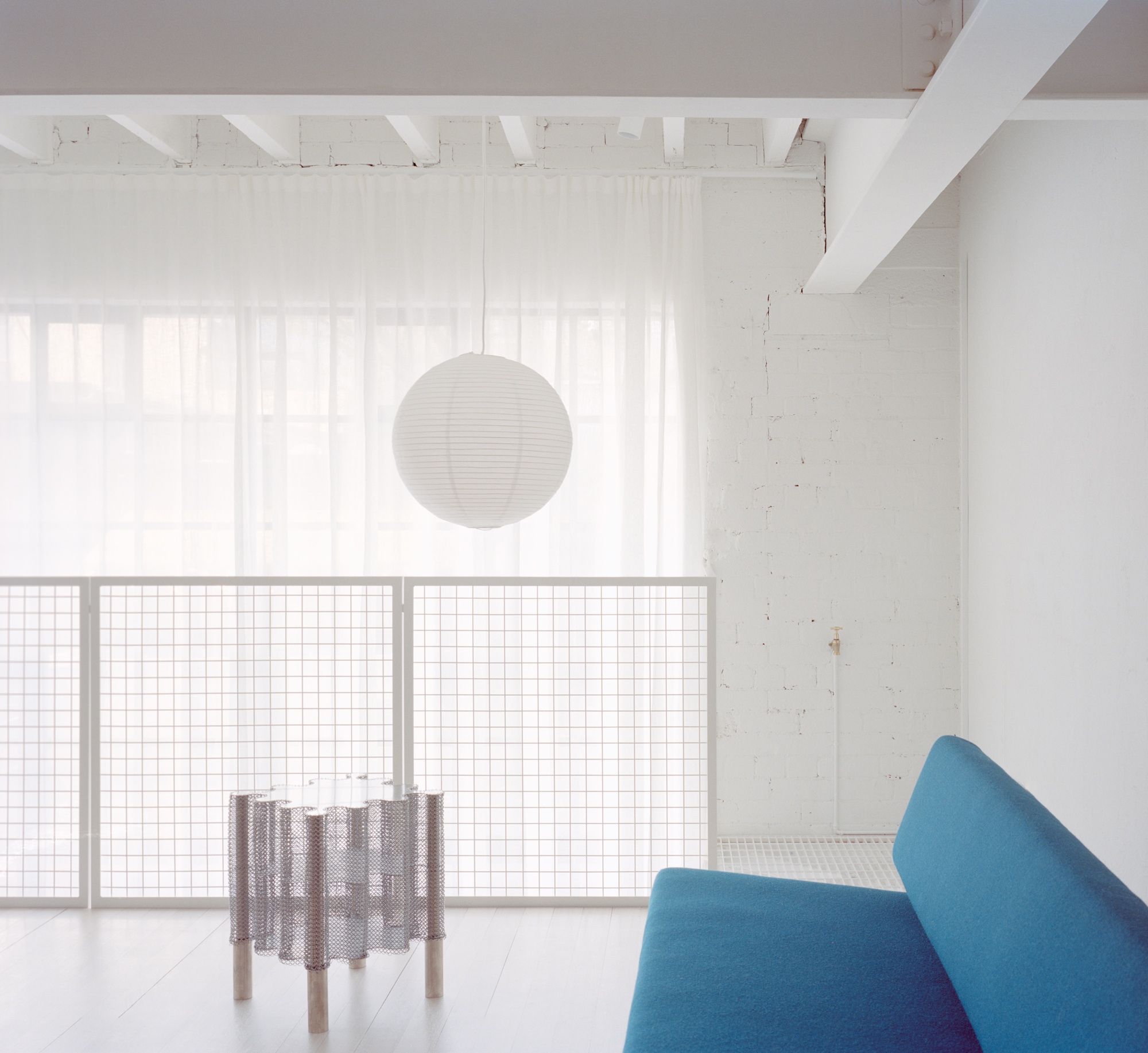 Living space with wire mesh balustrade, spherical pendant light, and sheer curtain filtering daylight from glazed openings