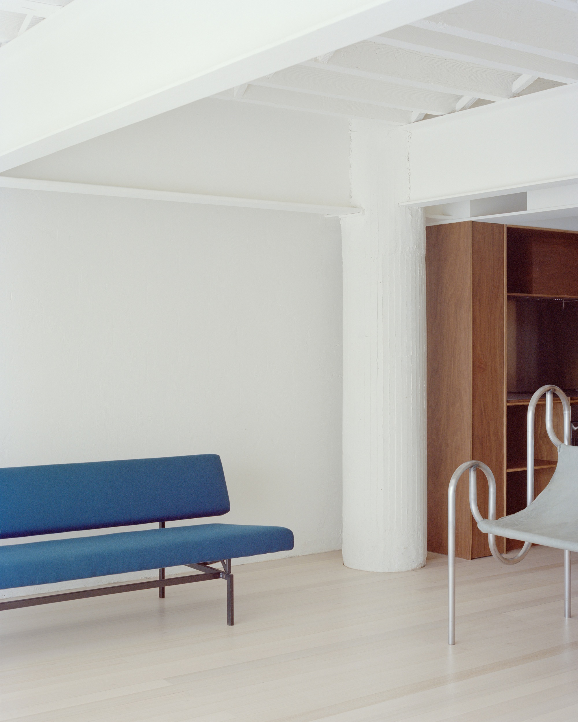 White room with exposed timber ceiling joists, blue upholstered sofa and cylindrical painted column