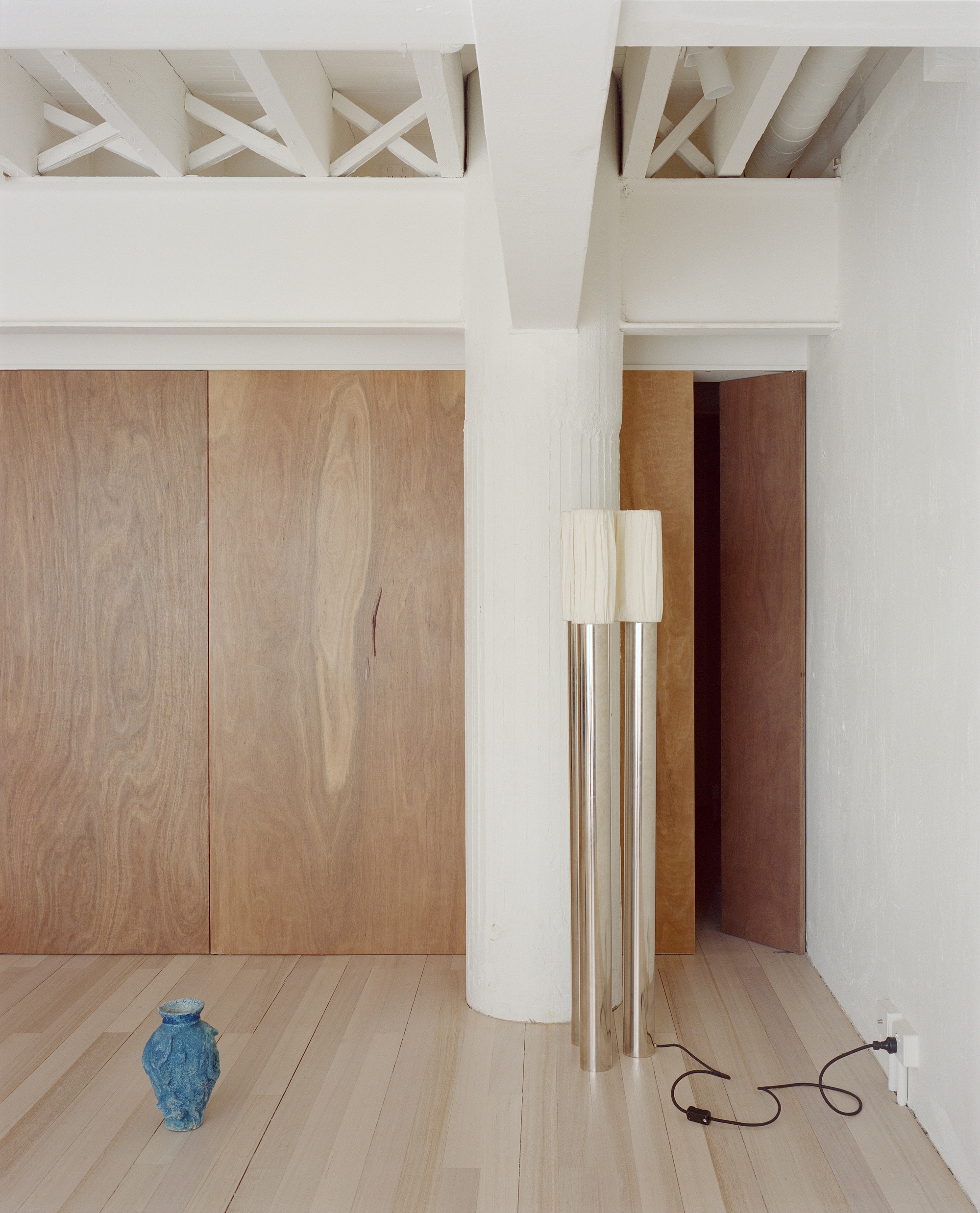 Room corner showing exposed timber ceiling structure, oak paneling, white column and blue ceramic vase