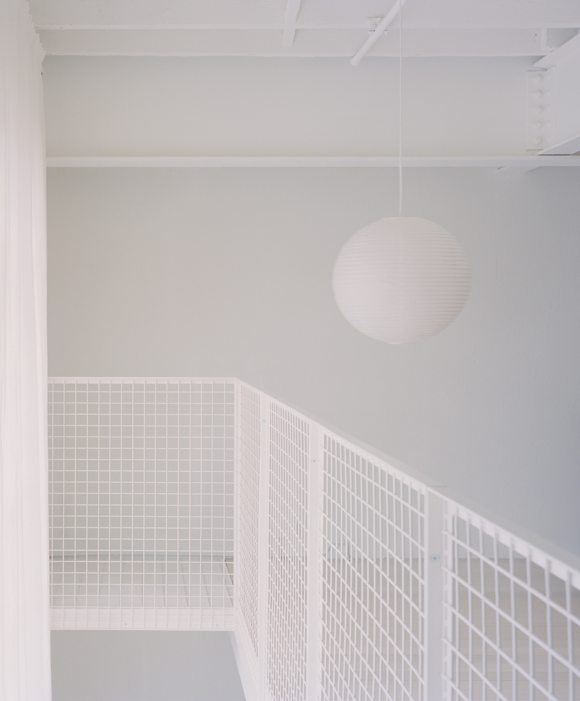 Upper level passage with white wire mesh railing and spherical pendant light under exposed joists