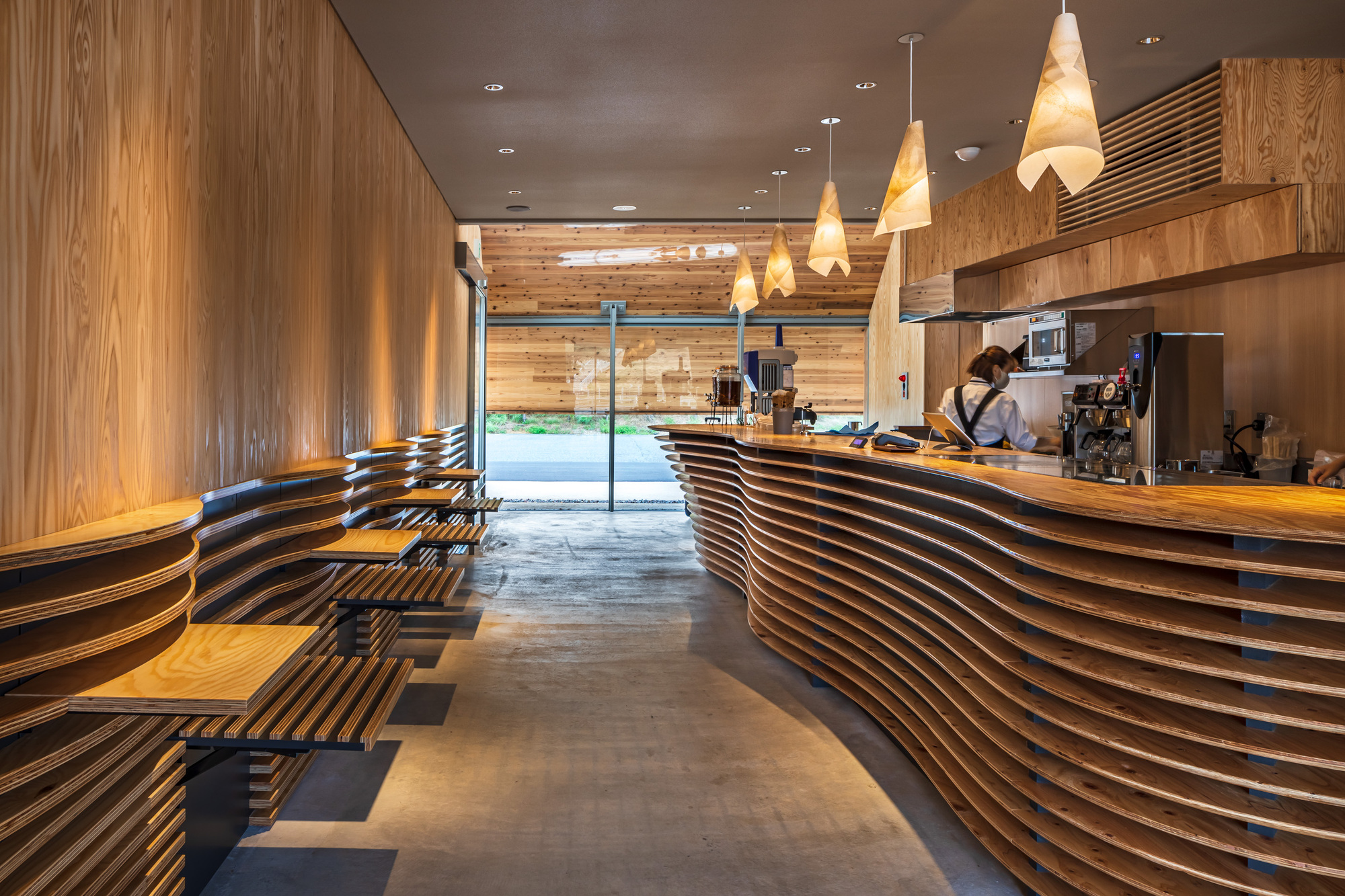 Interior cafe counter with horizontal slatted timber cladding and conical pendant lights overhead